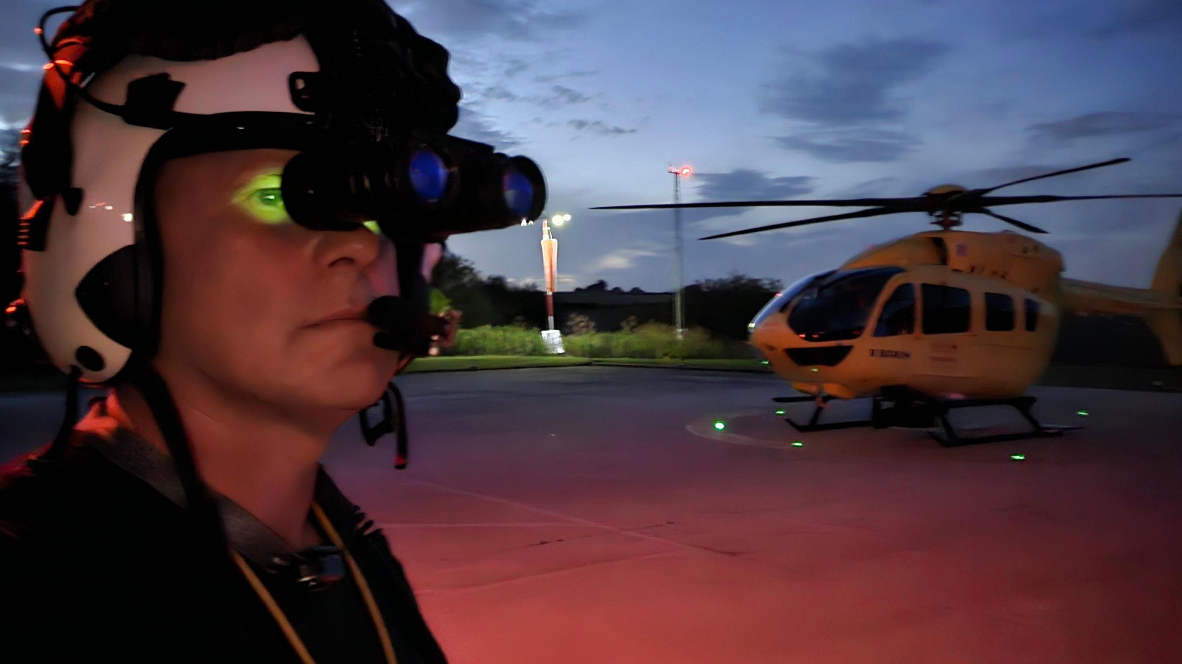 Yorkshire Air Ambulance Chief Pilot Owen McTeggart, wearing night vision goggle, with the air ambulance behind him.