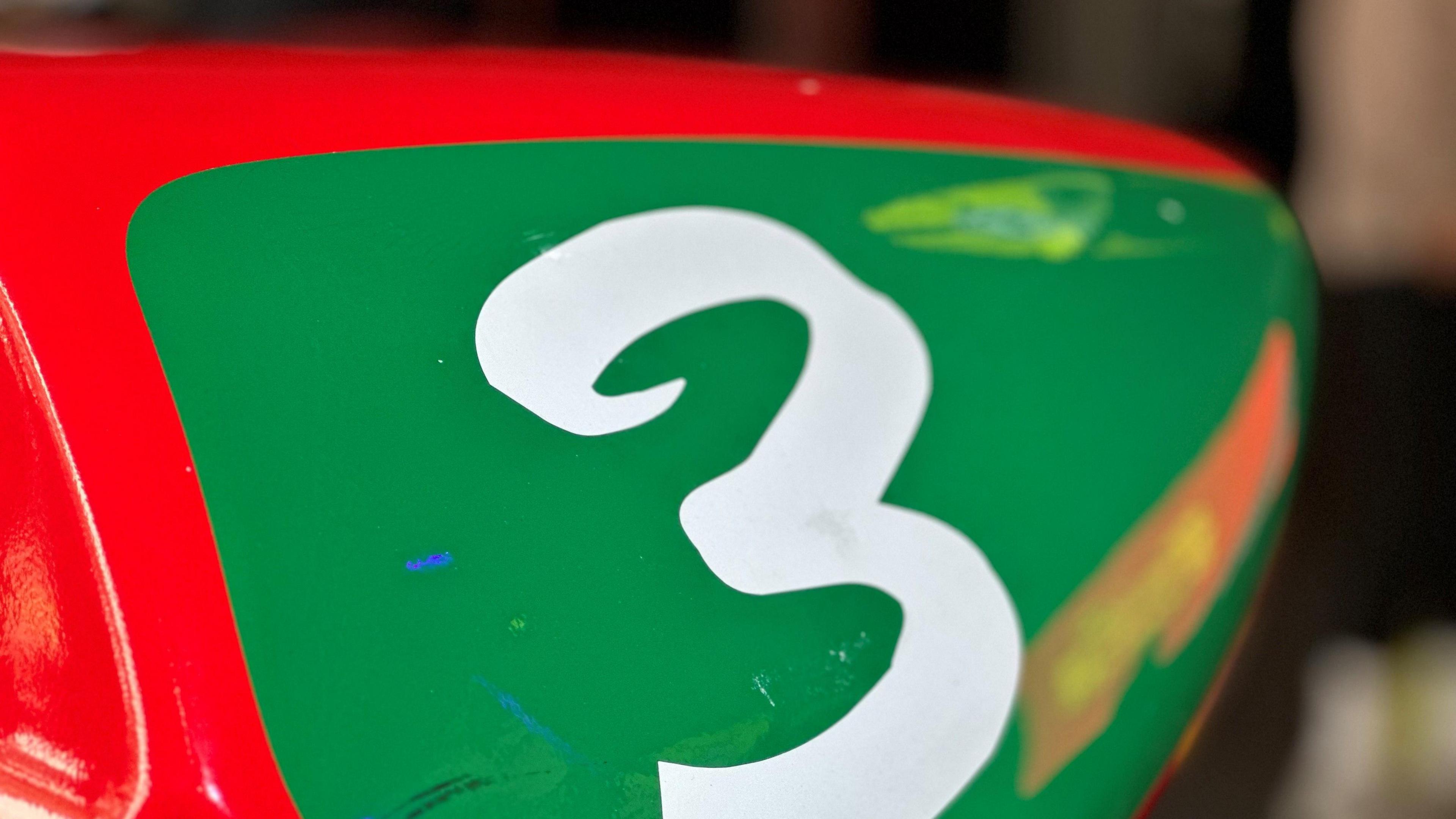 The number three in white on a green background on the rear of a red motorcycle.