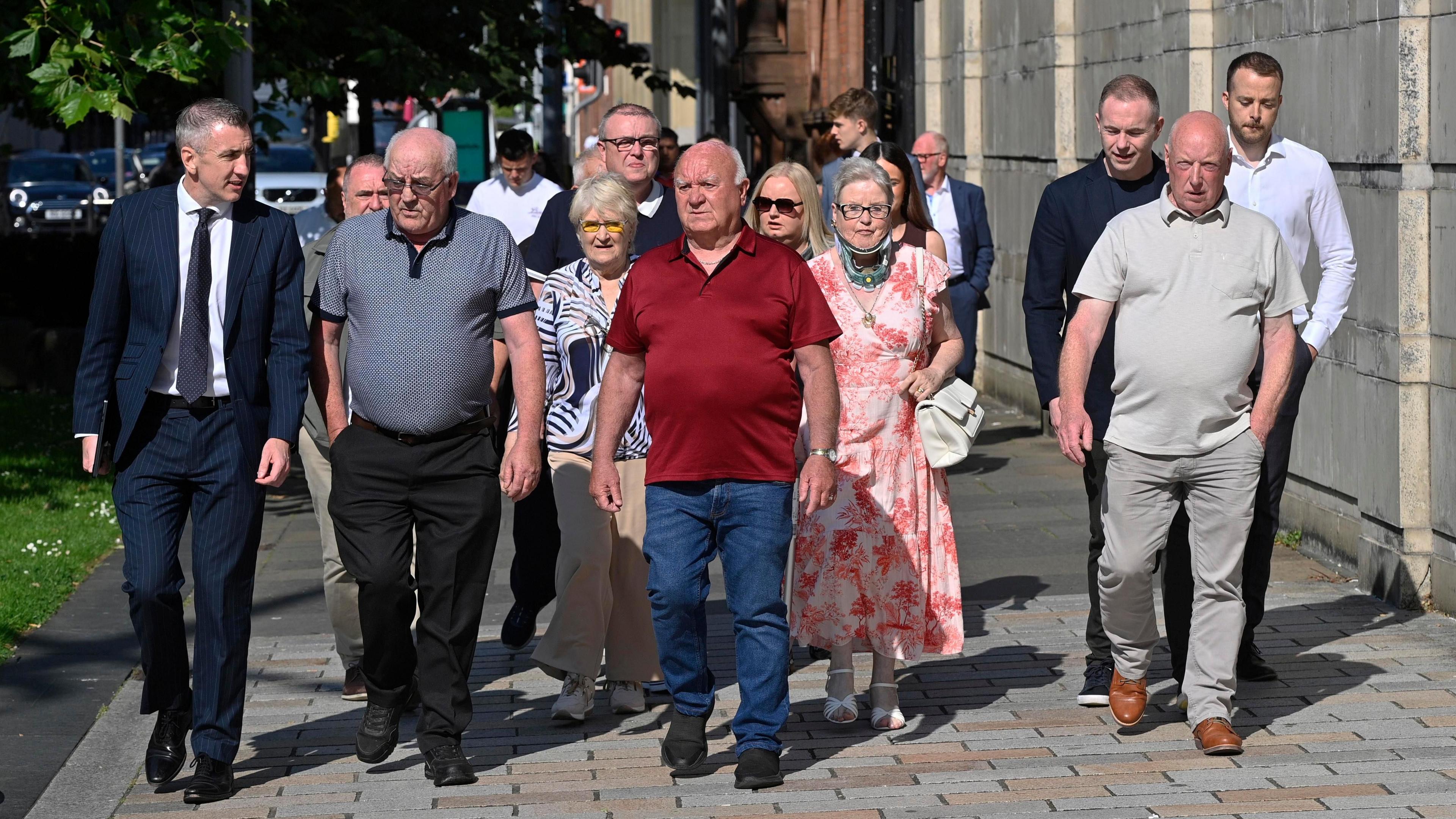 A group of people walking along a footpath in sunshine.