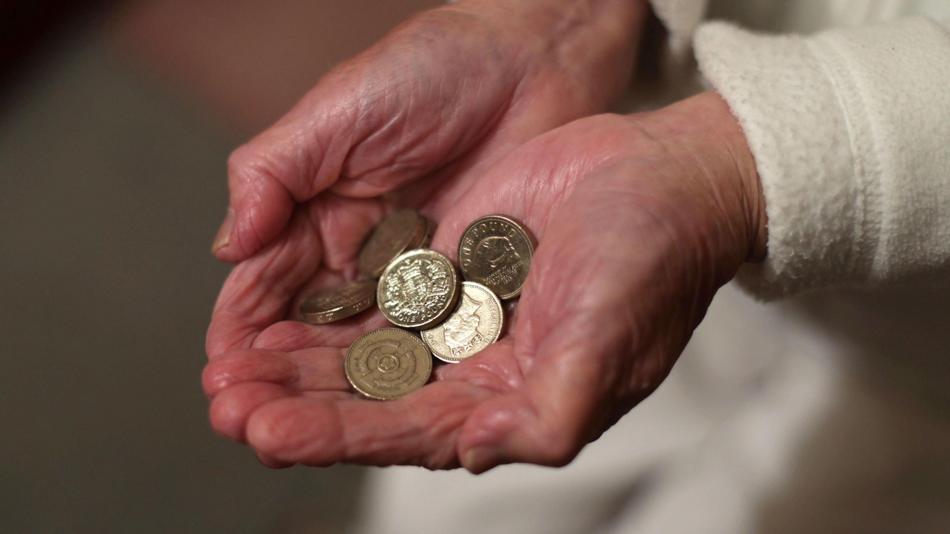 Close up of elderly person with wrinkled hands holding pound coins 