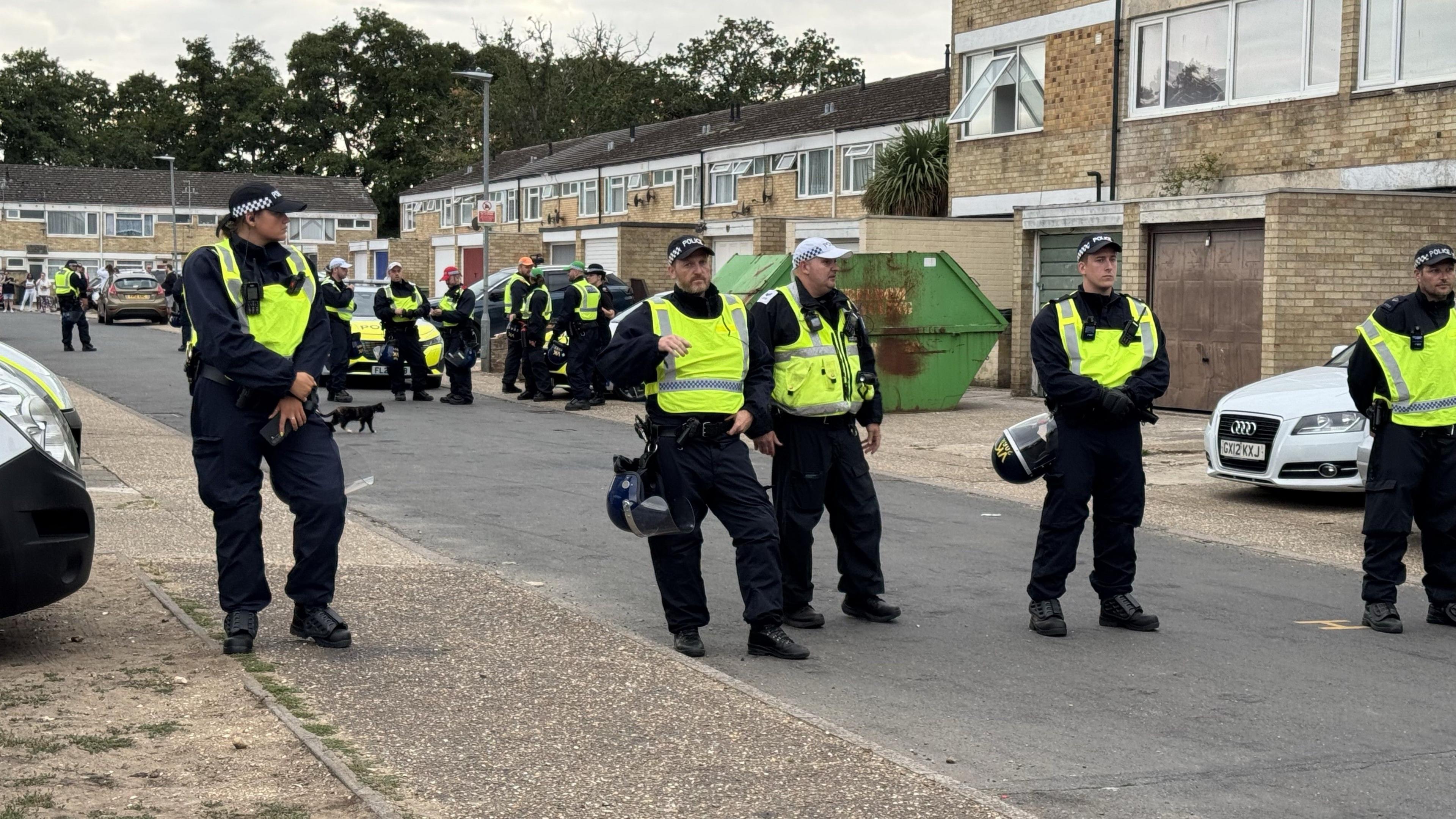 Group of police standing in a residential street holding helmets and wearing high vis protective vests