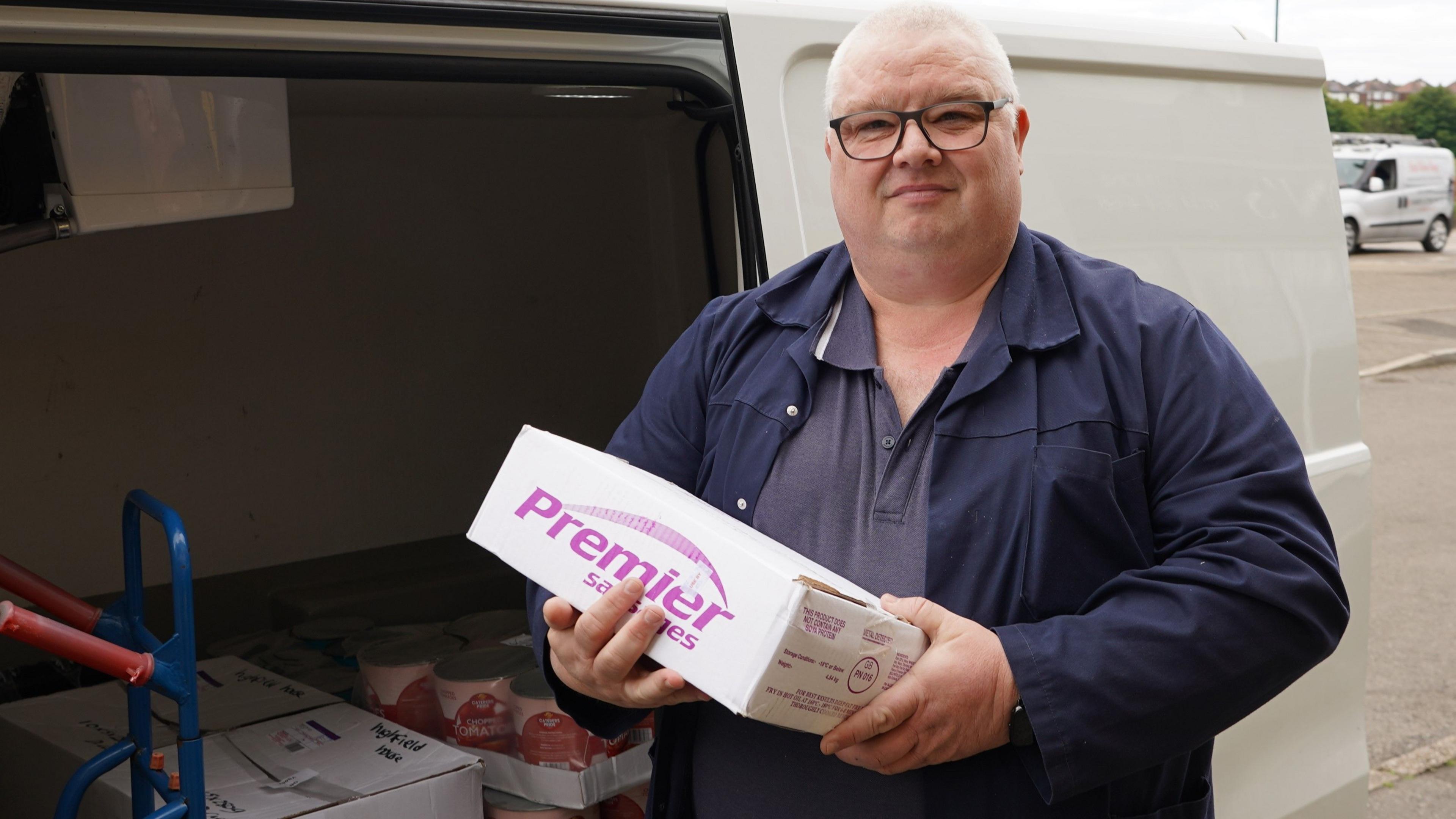 A man wearing blue overalls holds a white box of food