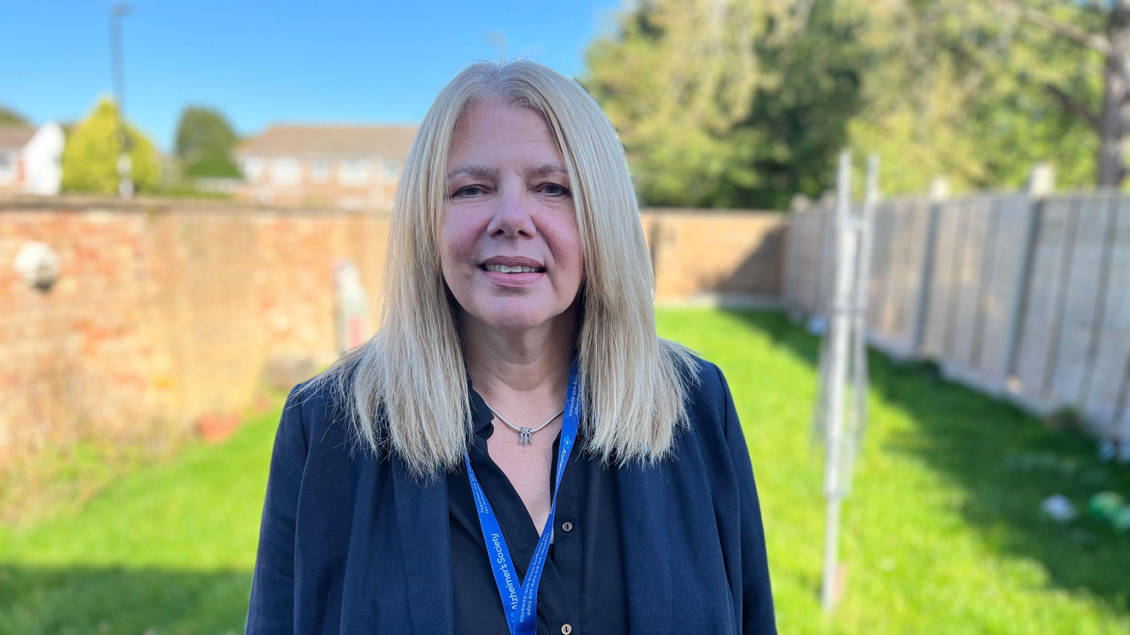 Ms Robertson is standing in a back garden. She has blonde hair and is wearing a blue jacket.