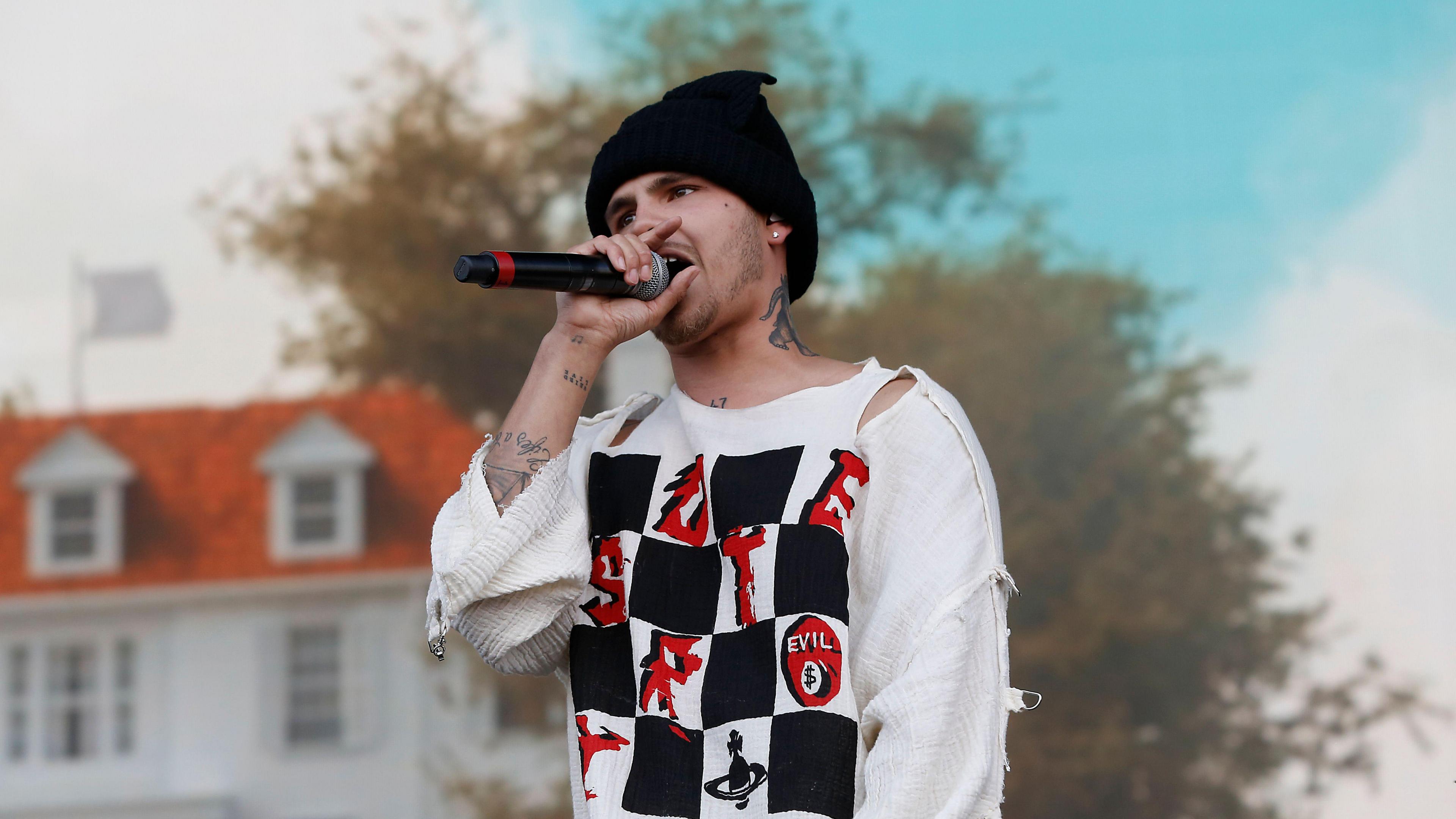 Slowthai performing with a microphone in his hand. He is wearing a black beanie hat and a ripped white shirt.