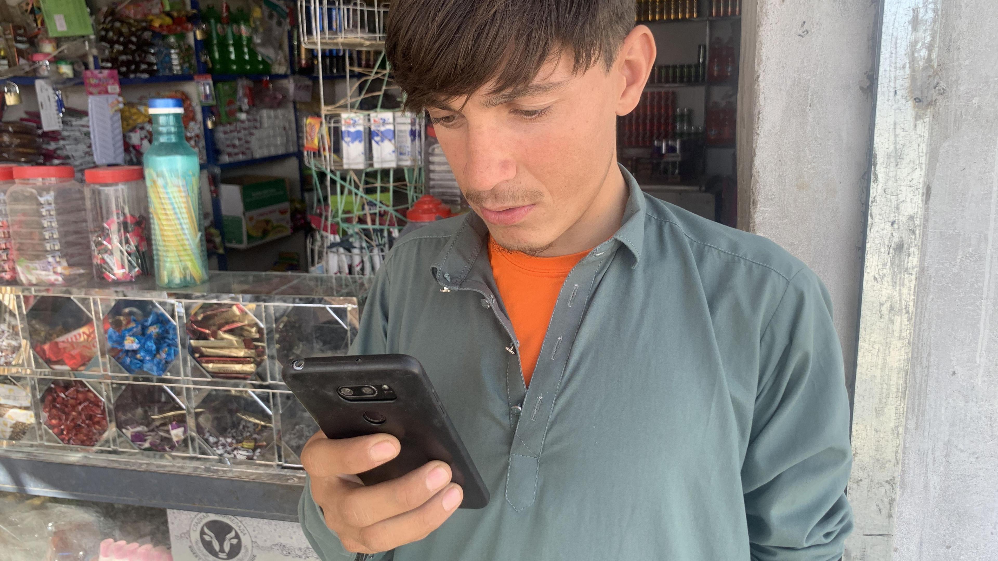 An Afghan man looks at his phone outside a convenience store