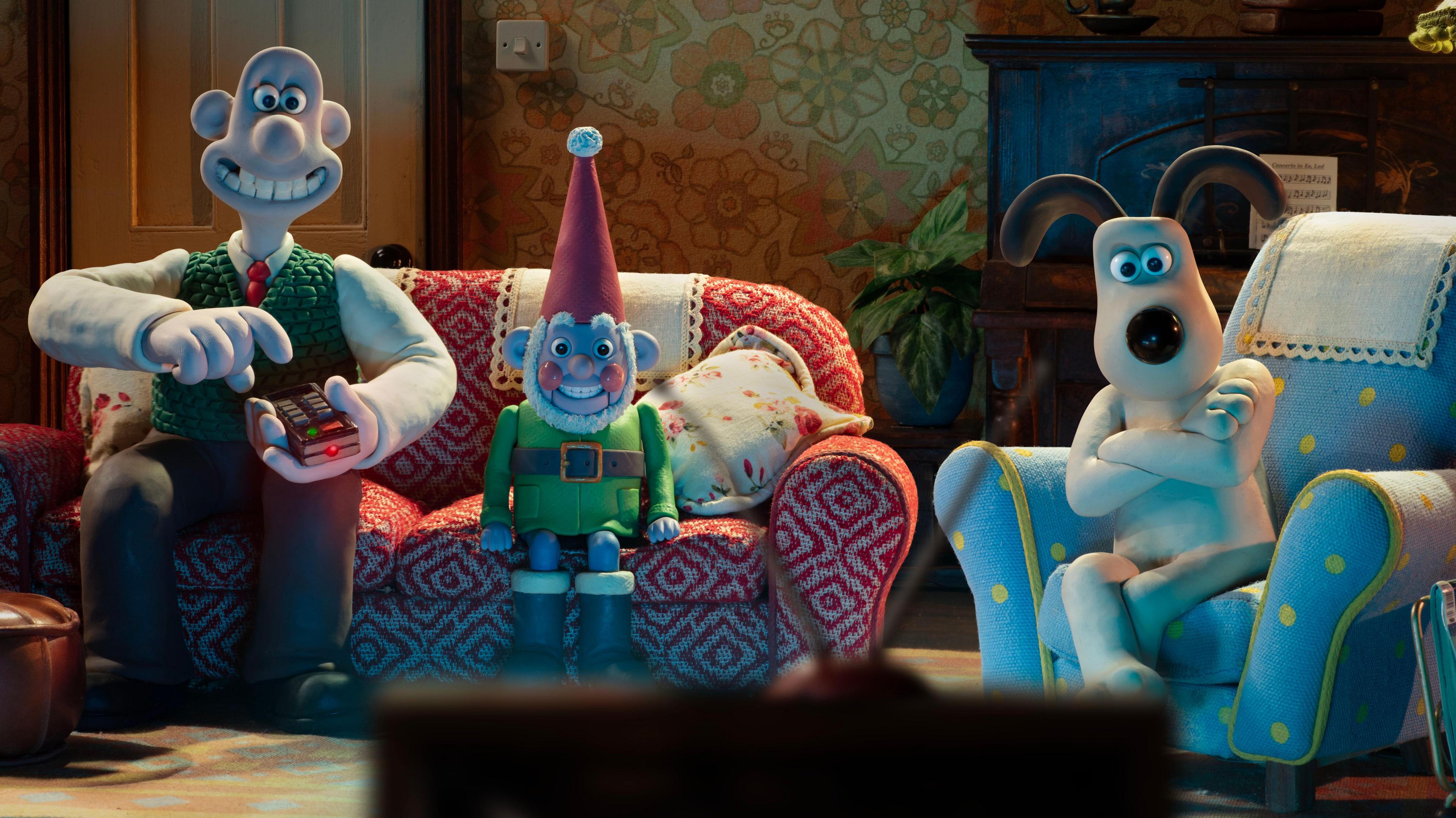 Wallace and Gromit are pictured in their living room, sitting on the sofa, along with a gnome.