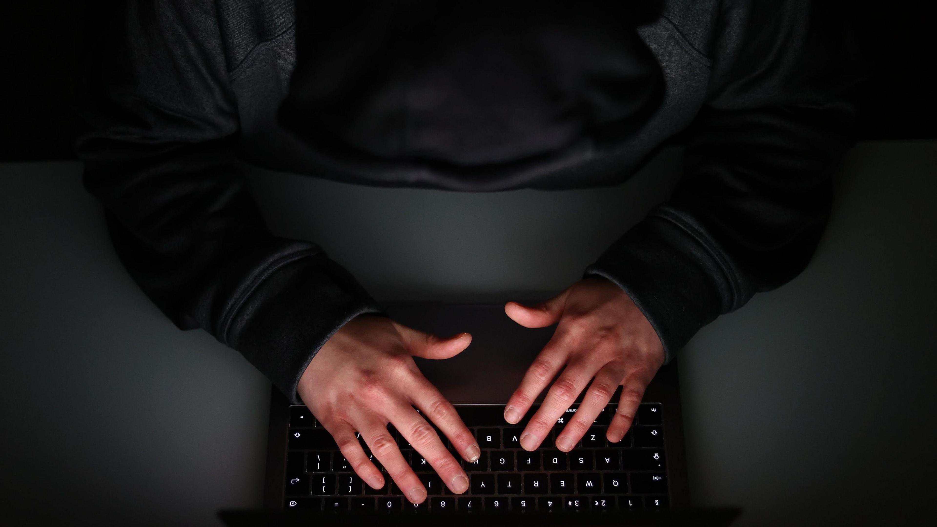 An ariel shot of a person typing on a laptop wearing a black hoodie. You can't see any features.