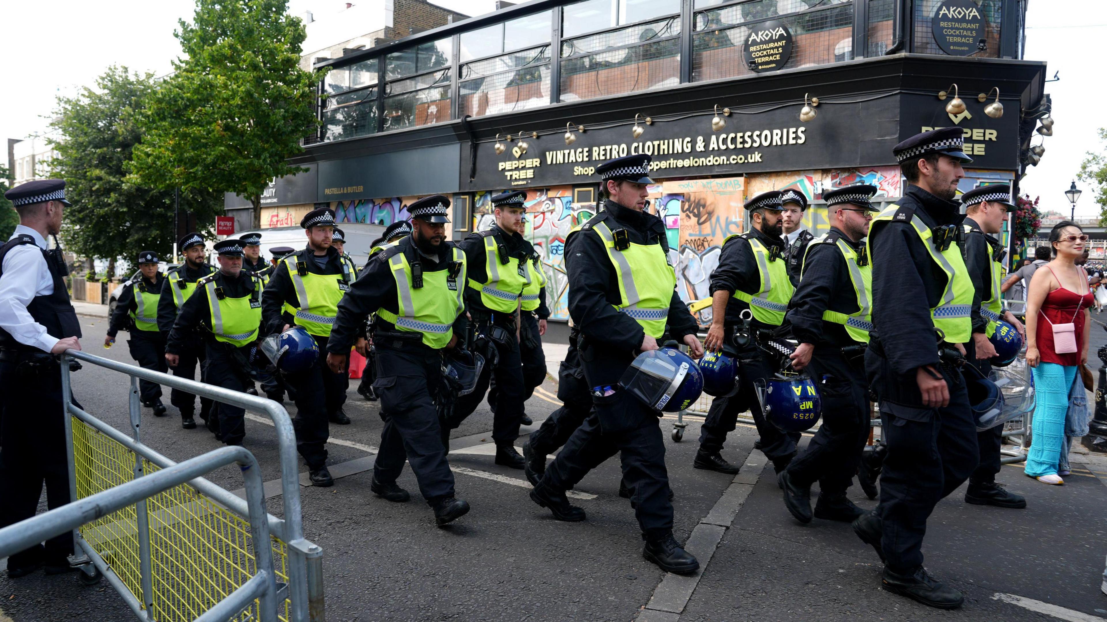 A group of police officers walk through the streets of Ladbroke Grove. They are holding blue police helmets in their hands. 