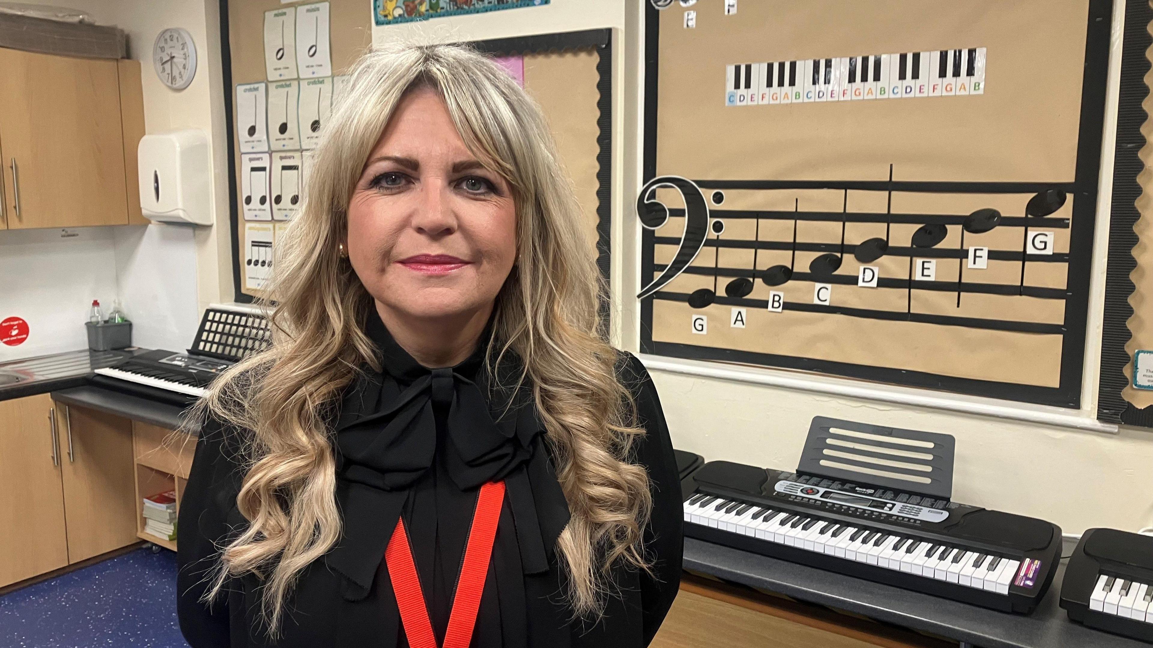 Photograph of a headteacher in a classroom in Stockport, with keyboards in the background and a bass clef on music sheet - reading G,A,B, C, D, E, F, G