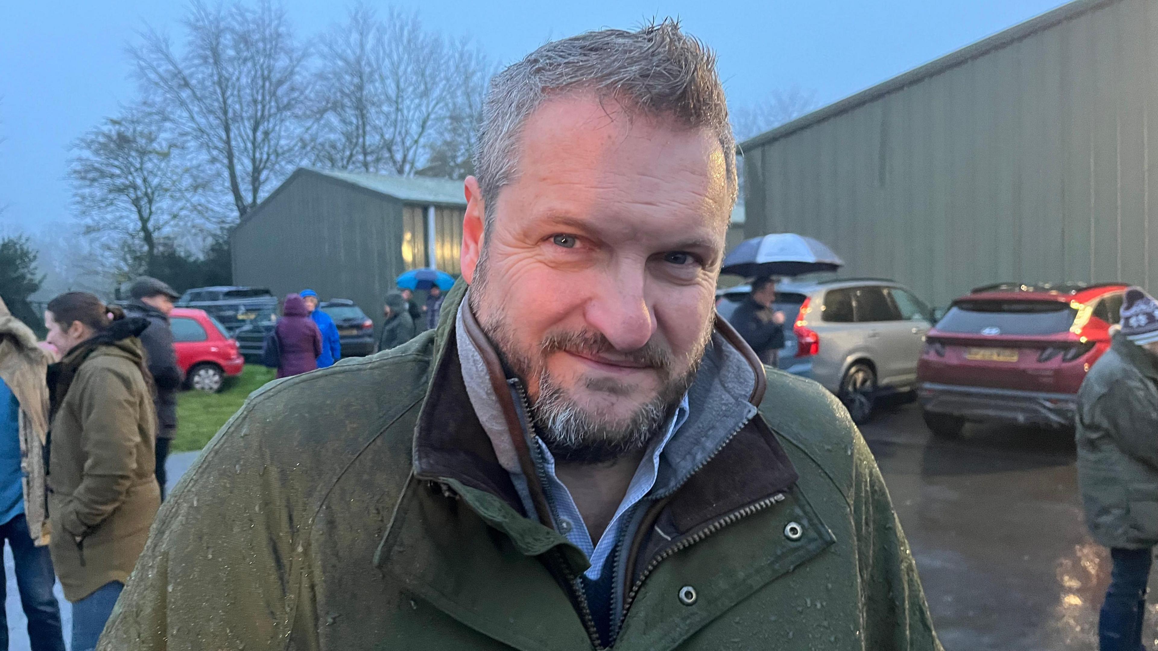 Tim Porter standing in the rain with other farmers gathered behind him in a car park, ready to leave for London