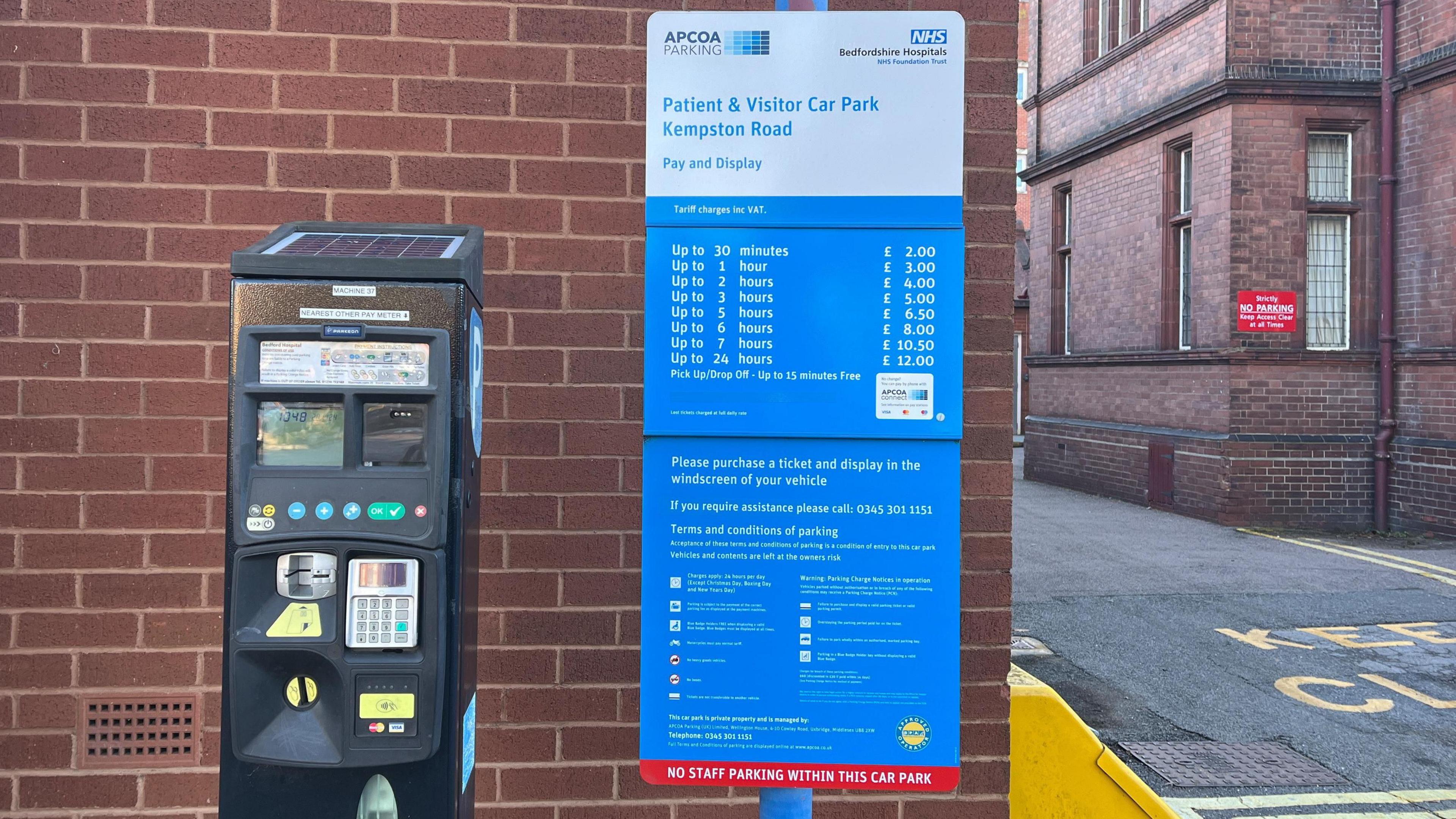 A parking meter with a notice next to it detailing the various charges within the hospital grounds.