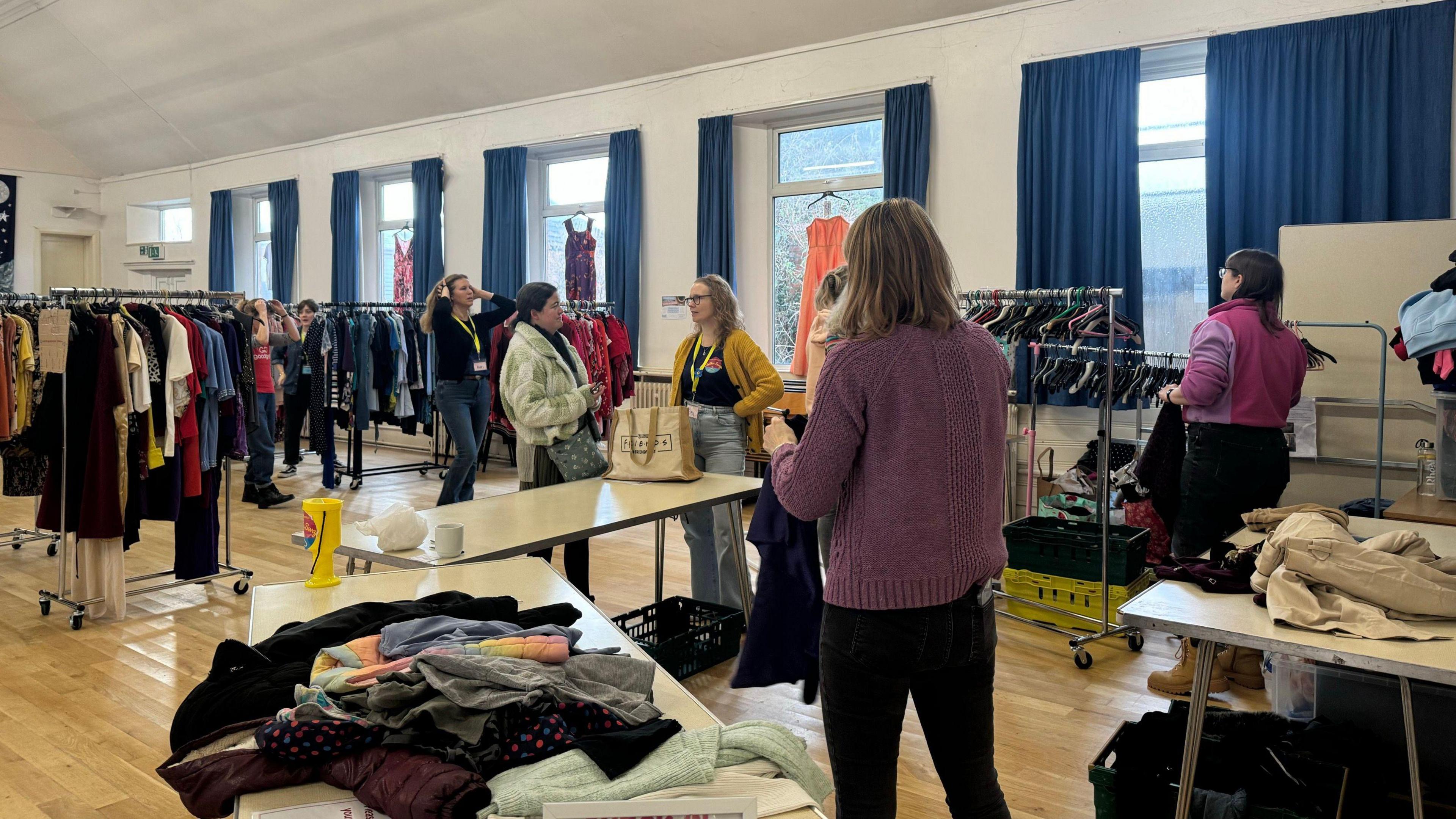 Volunteers sort clothes on tables and rails in a church hall.