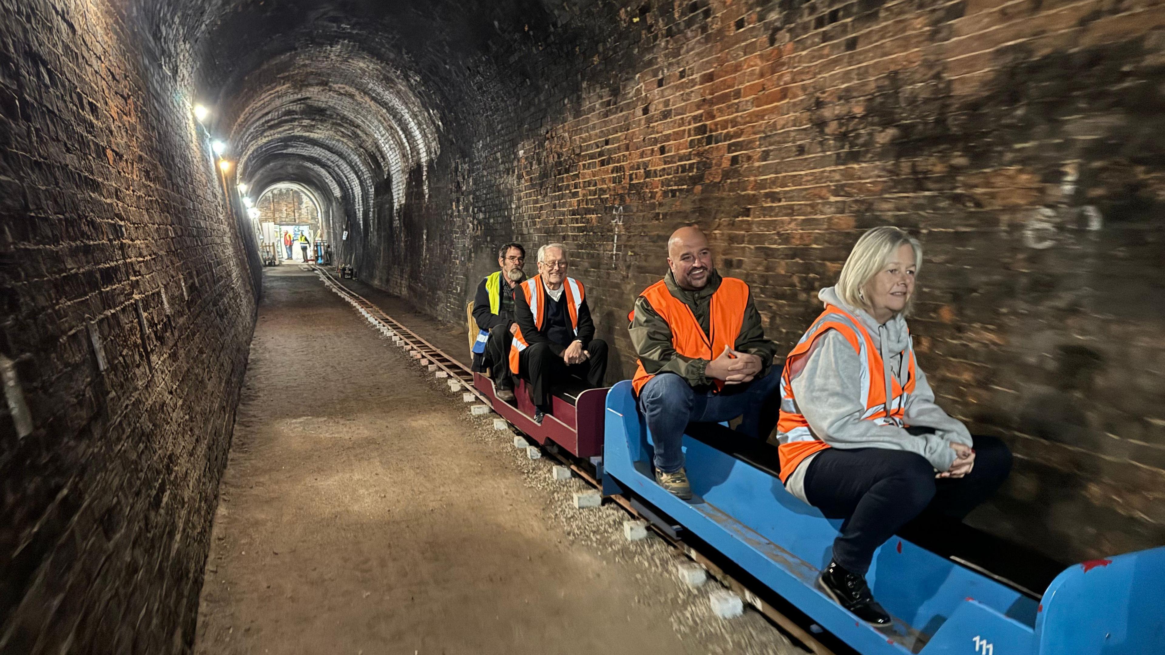 A miniature railway with four people wearing fluorescent jackets in a long tunnel