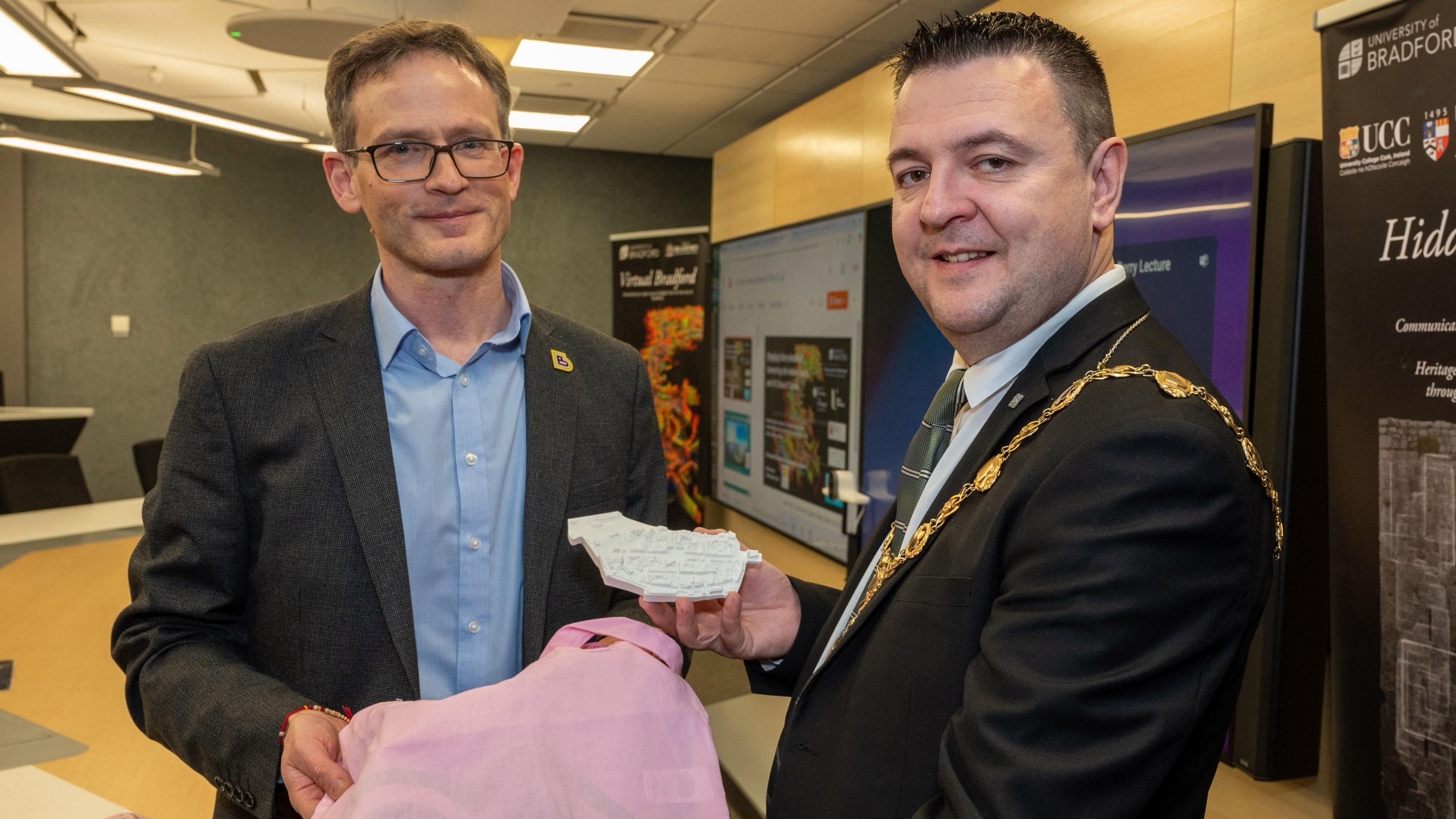 The mayor of Derry and Strabane councillor Ruairi McHugh (Right), is wearing his mayoral chains and is in a black suit with green tie. Beside him is professor Andrew Wilson (left) from the University of Bradford, in a blue shirt and grey jacket.
