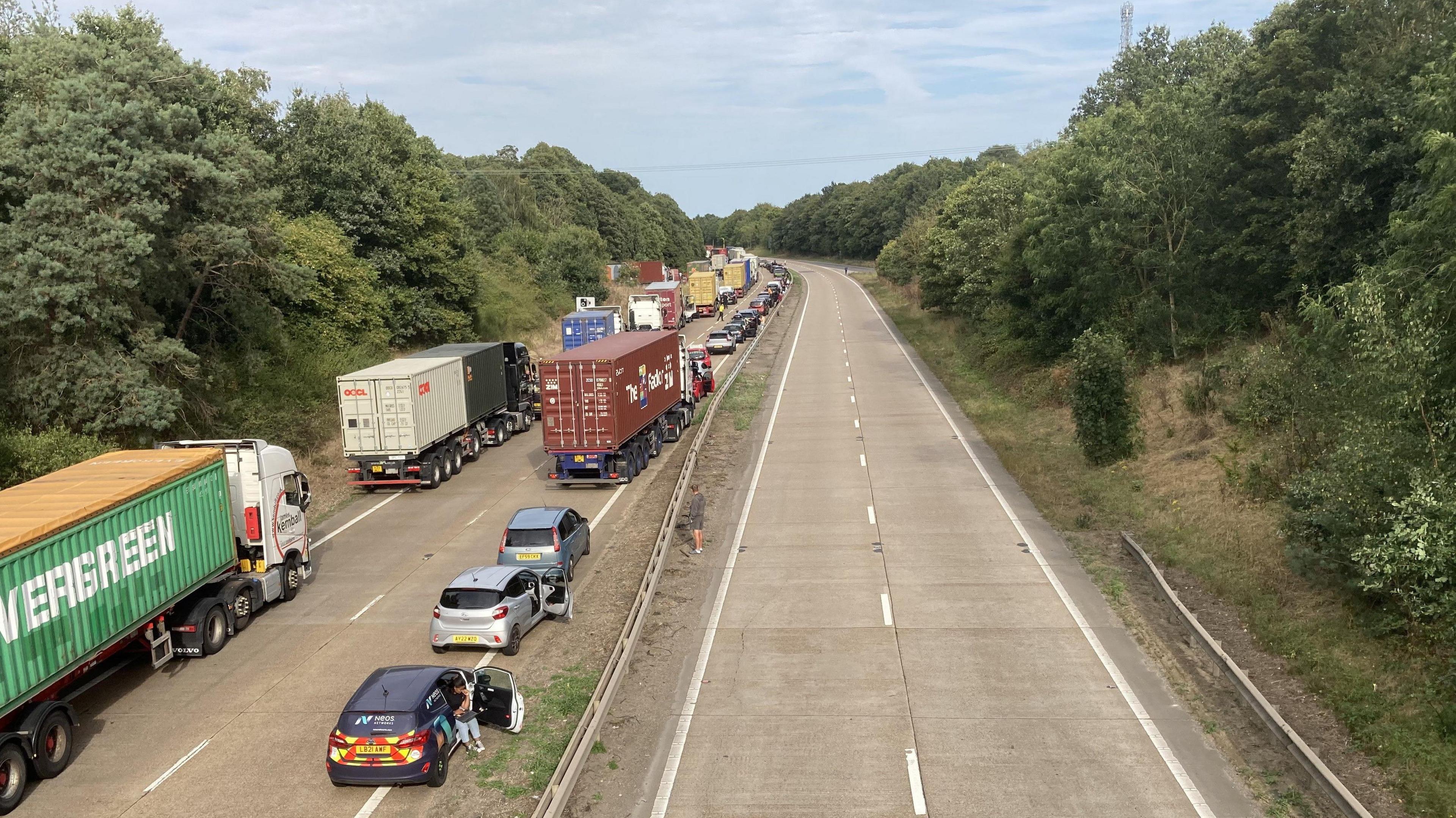 A view of the A14 near junction 56 near Ipswich. The right hand side of the dual carriageway is empty of cars. The left hand side has queues of vehicles stationary on the road.