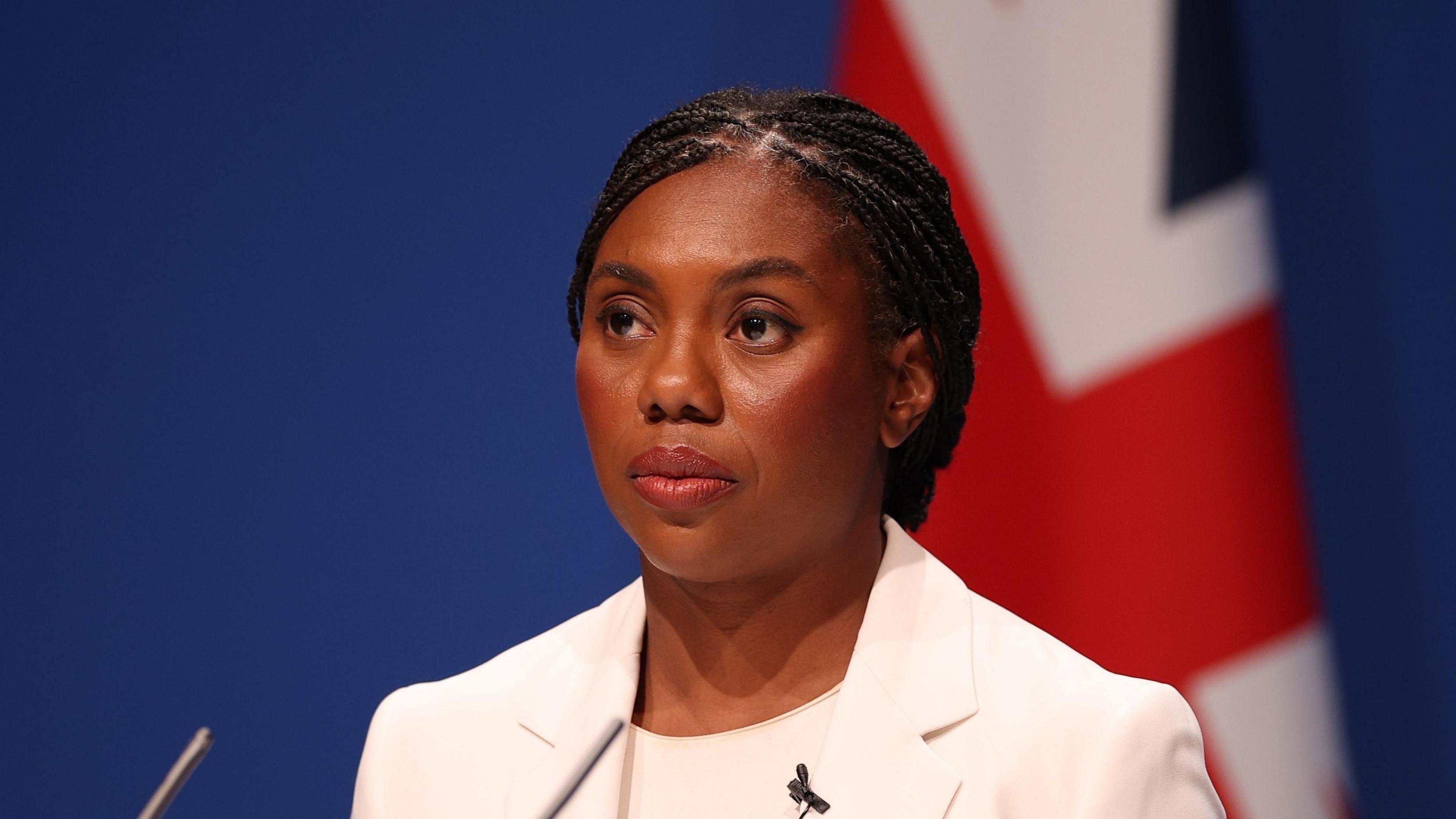 British Conservative Party Leader Kemi Badenoch delivers a speech during the Conservative Party Conference in Manchester, Britain. She wears a front page and stands in front of a Union Jack.
