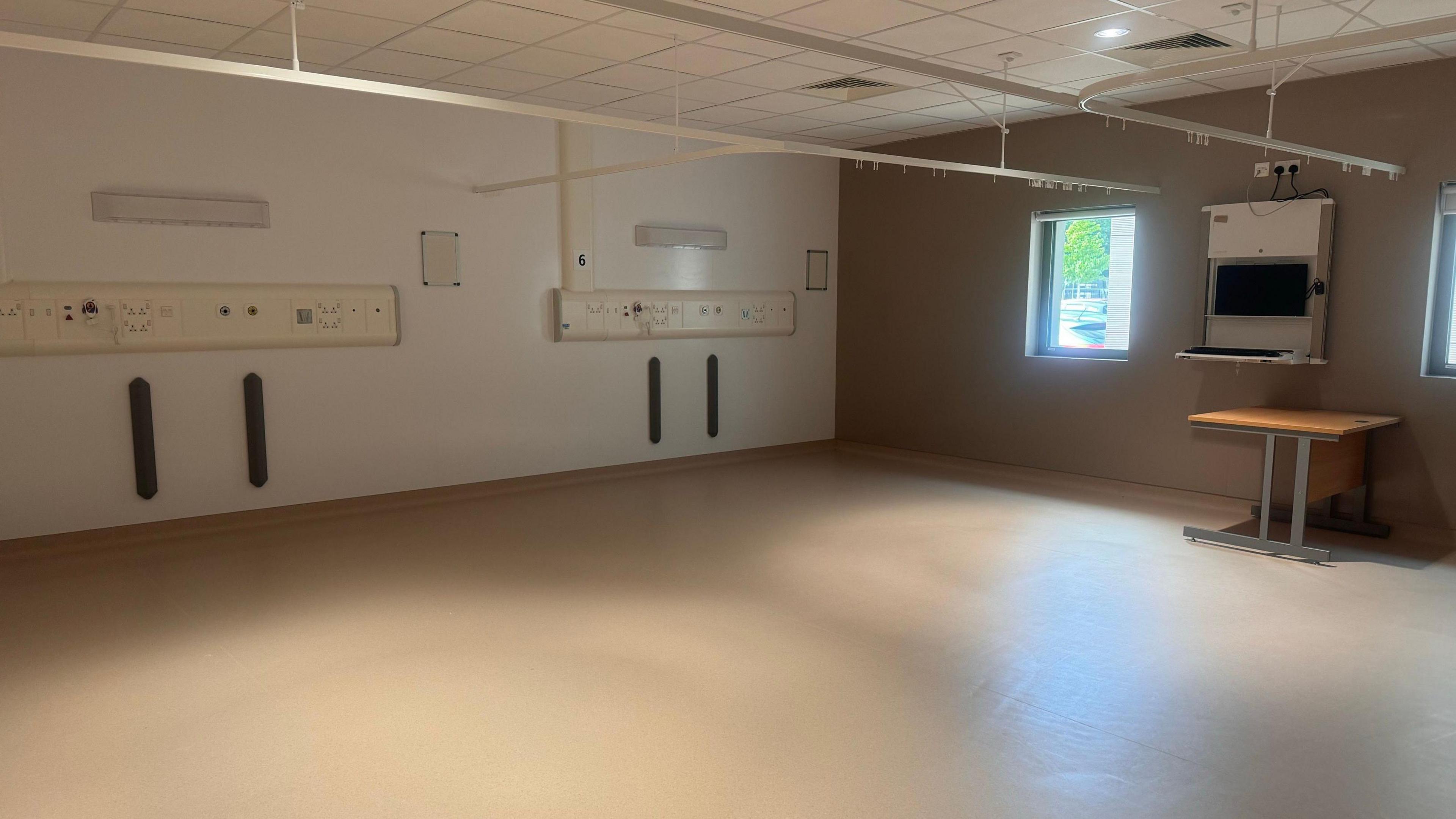 A large empty hospital room with curtain rails and beige coloured floors