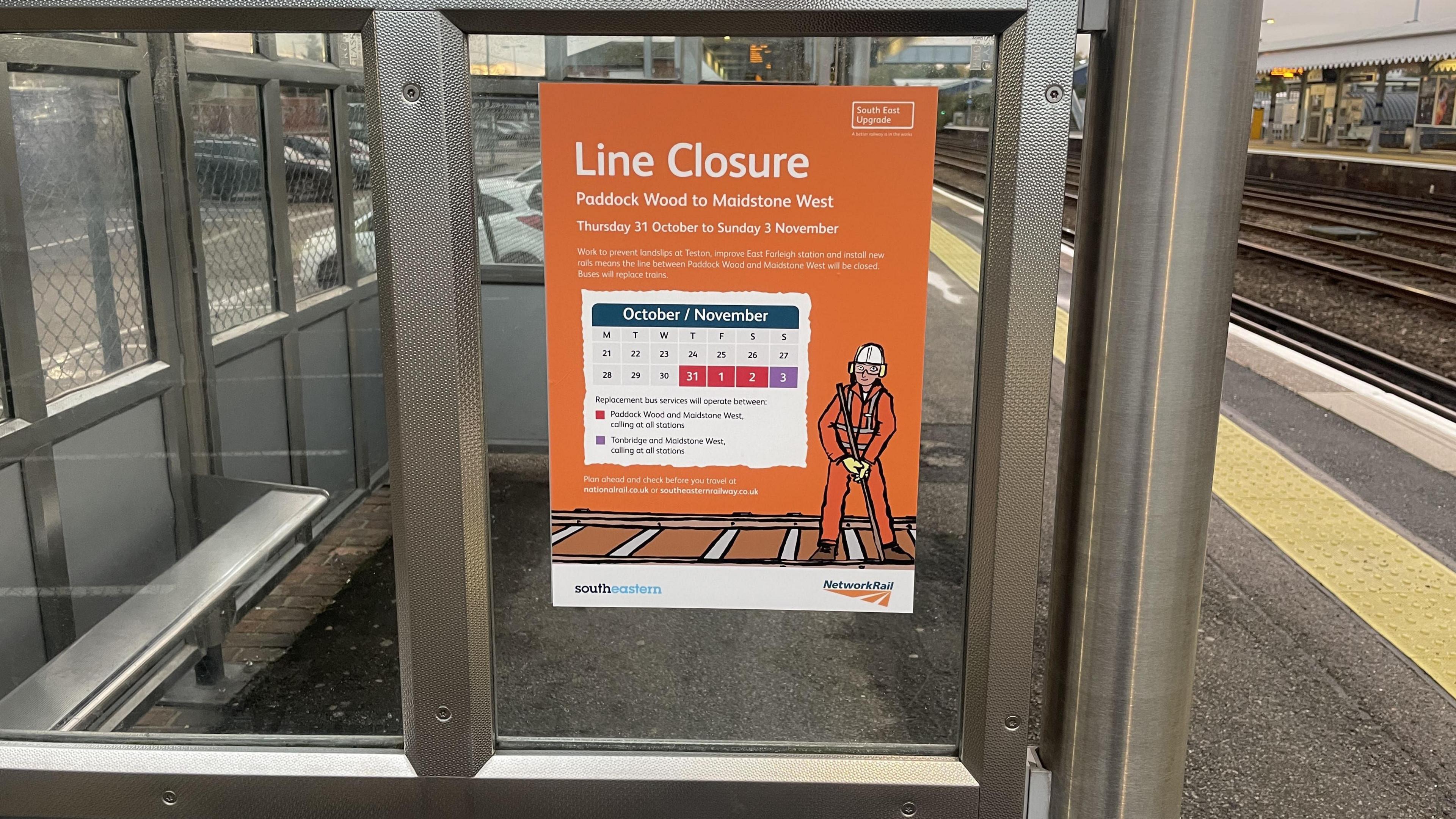 An orange sign on a shelter at Paddock Wood train station which has a calendar on, in different colours (white, red and purple) telling passengers what trains will and won't be running