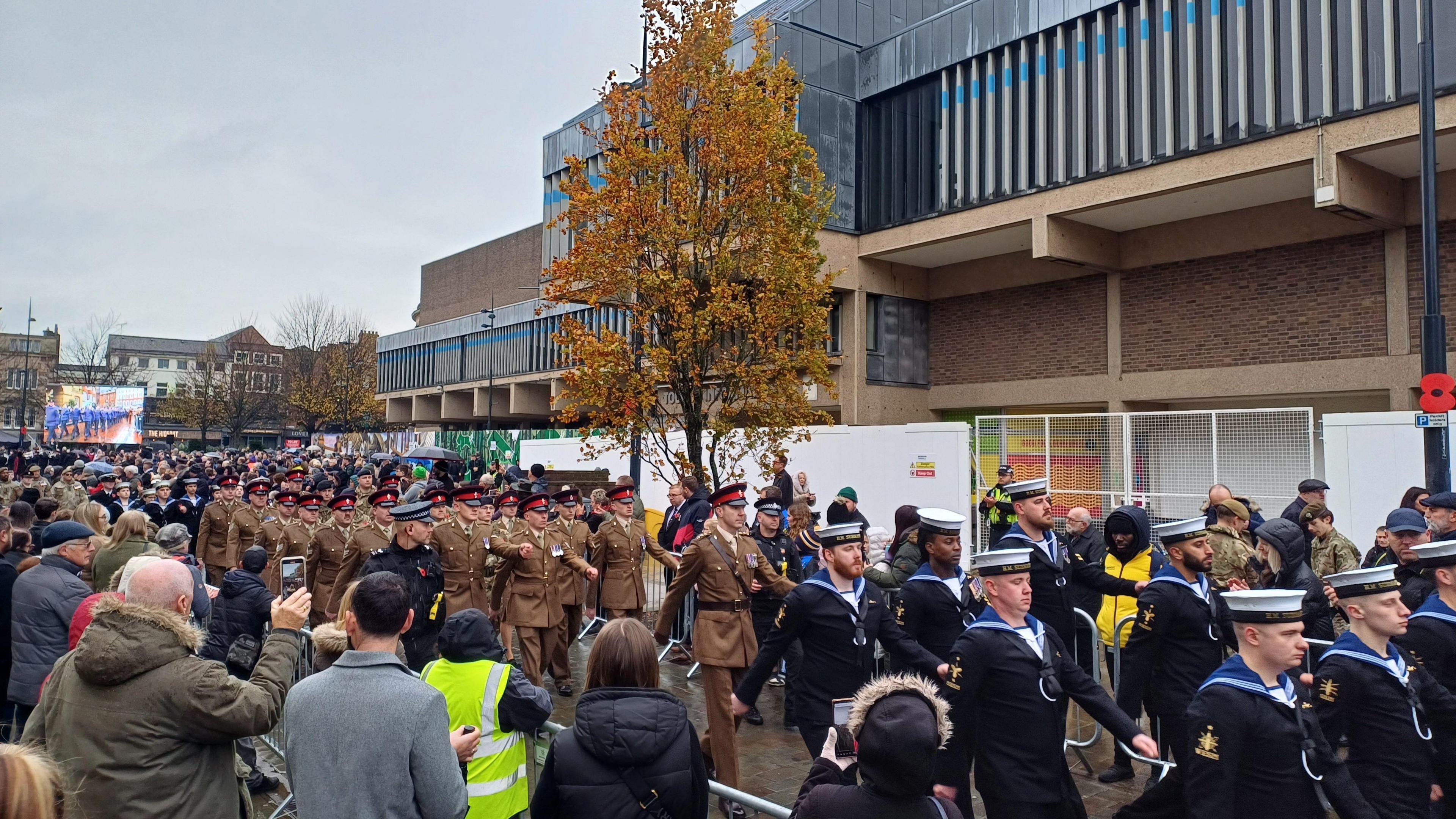 A parade through the streets of Derby with a crowd watching behind a fence