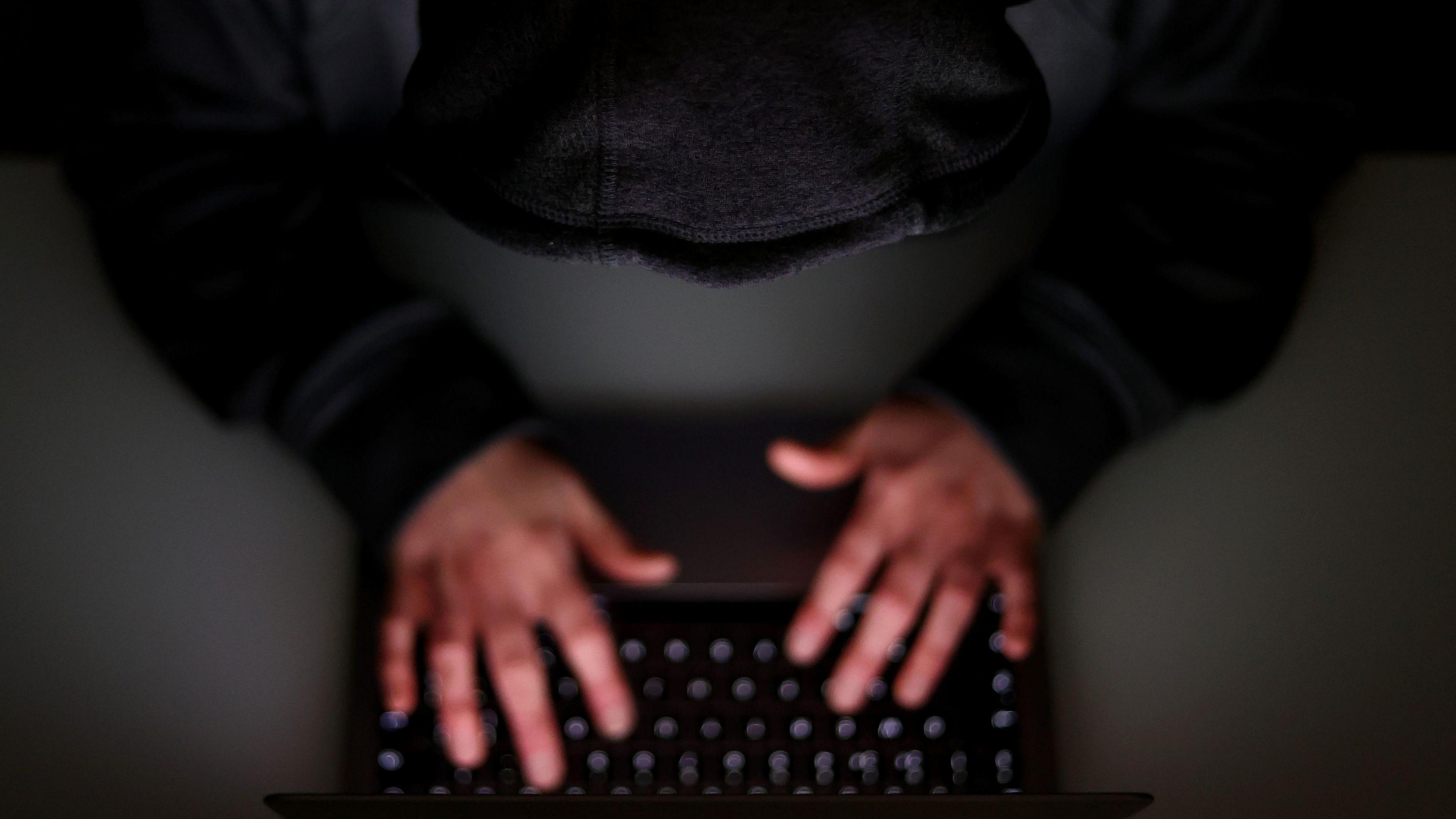 A man with his hands on a keyboard, wearing a black hoodie. 