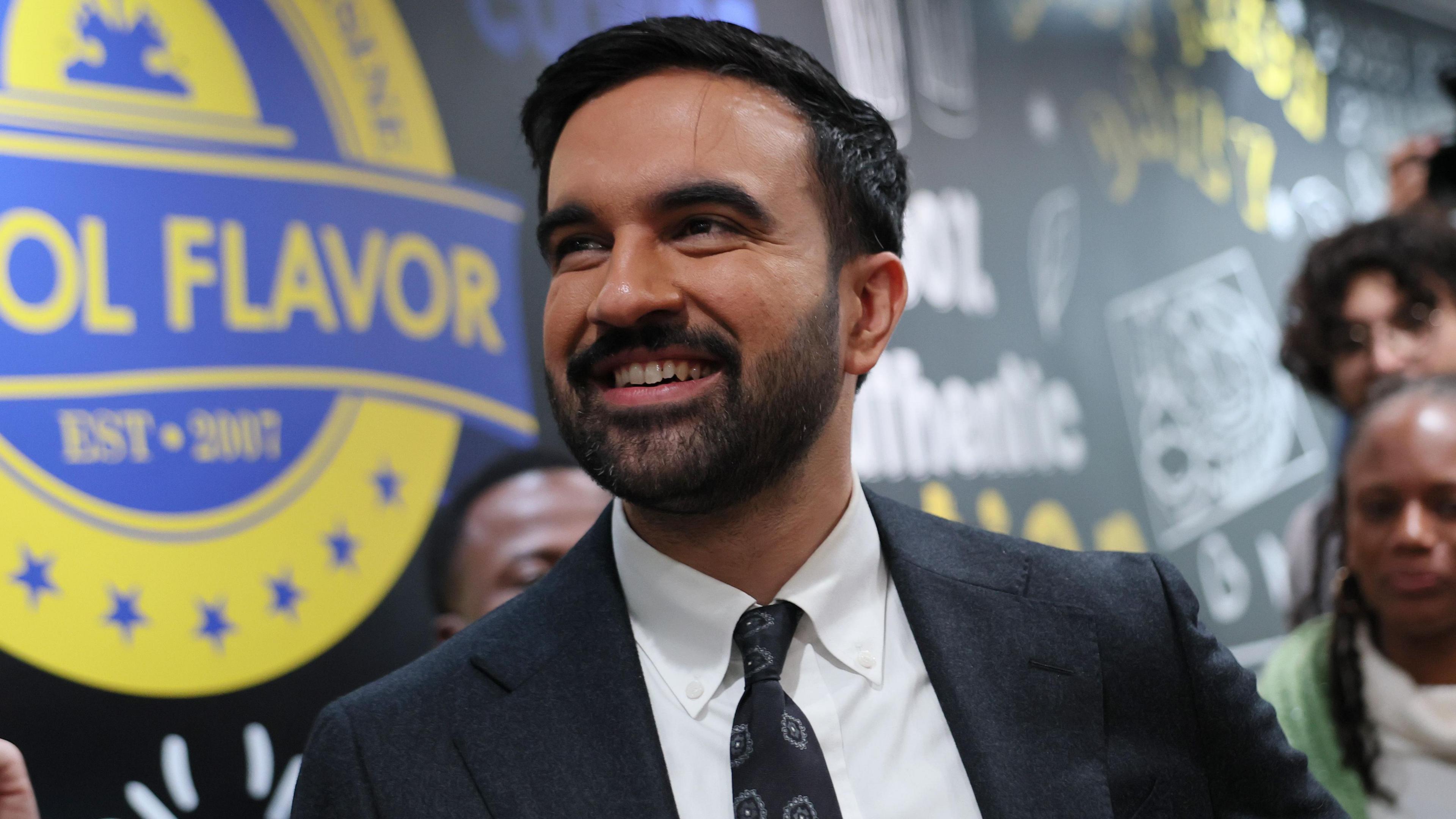 Zohran Mamdani, a young, bearded man in a suit and tie, looks at the menu inside of Kreyol Flavor as he takes a tour of New York on 25 October