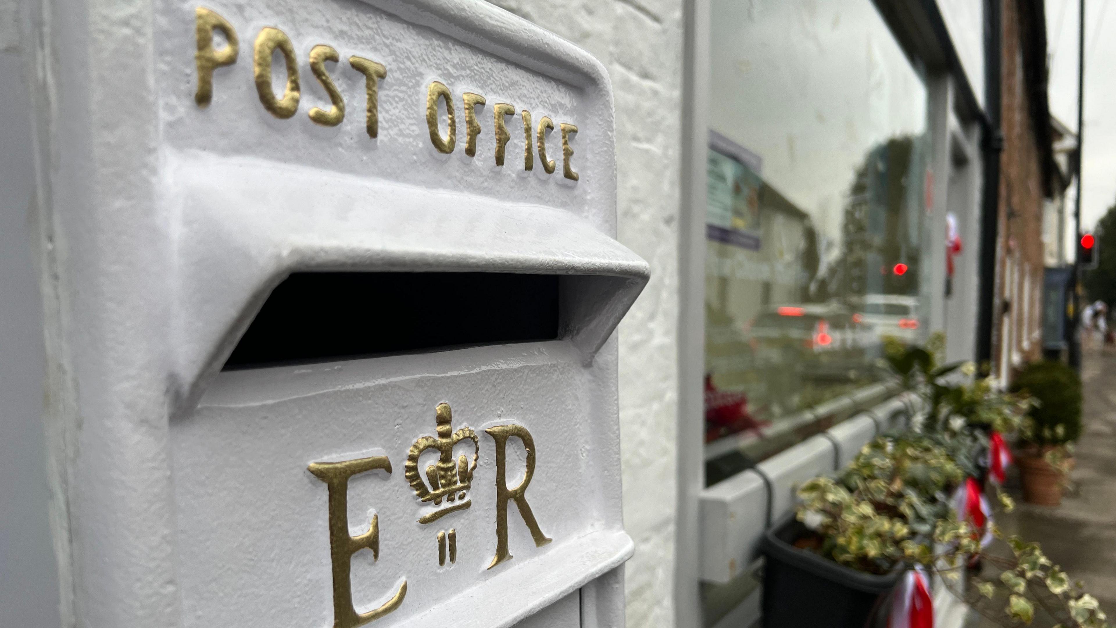 The top of a classic post box, but painted white with gold lettering.