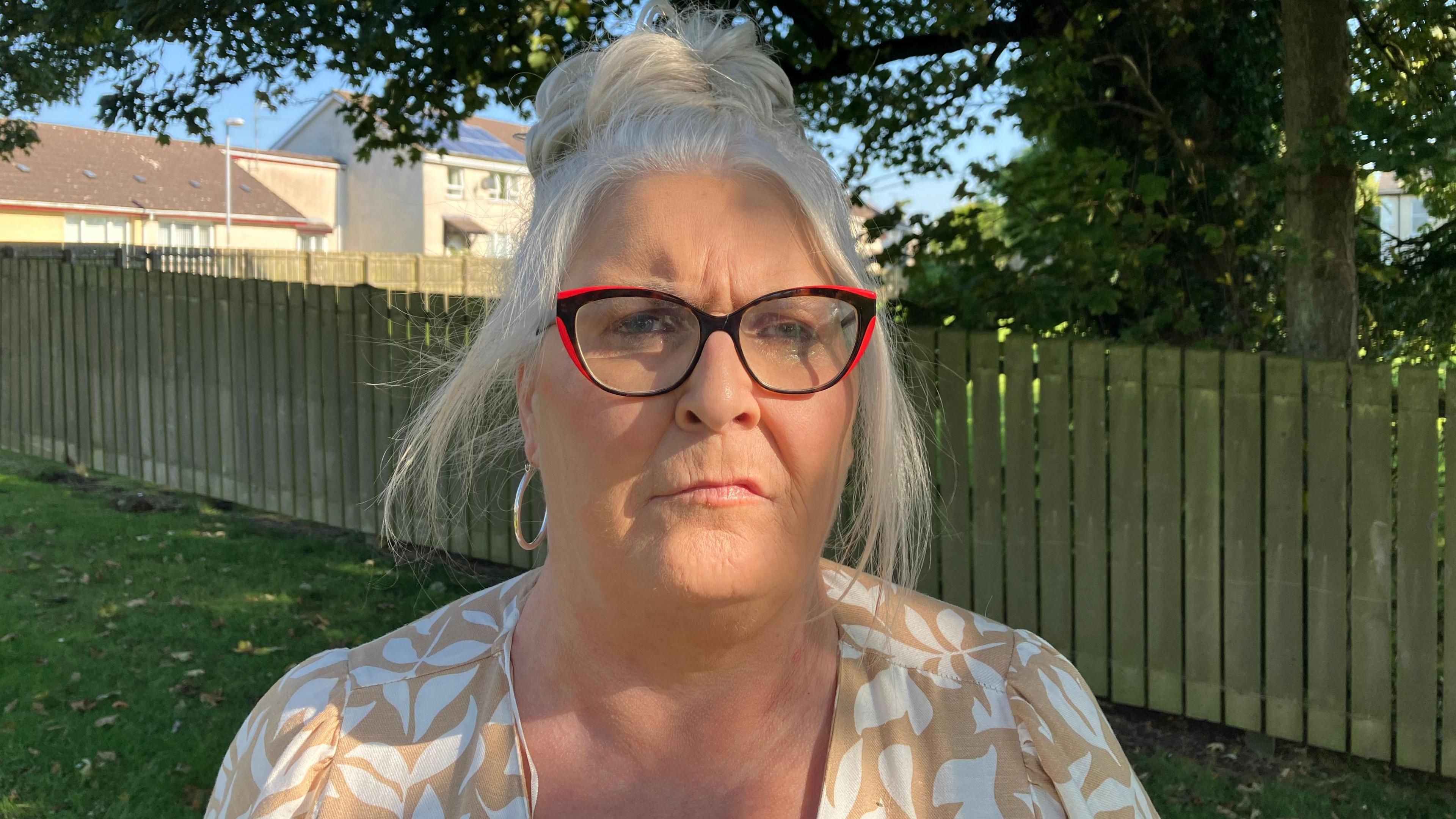 Kathleen  Arkinson  stands in front of a fence, with grass and trees in the background