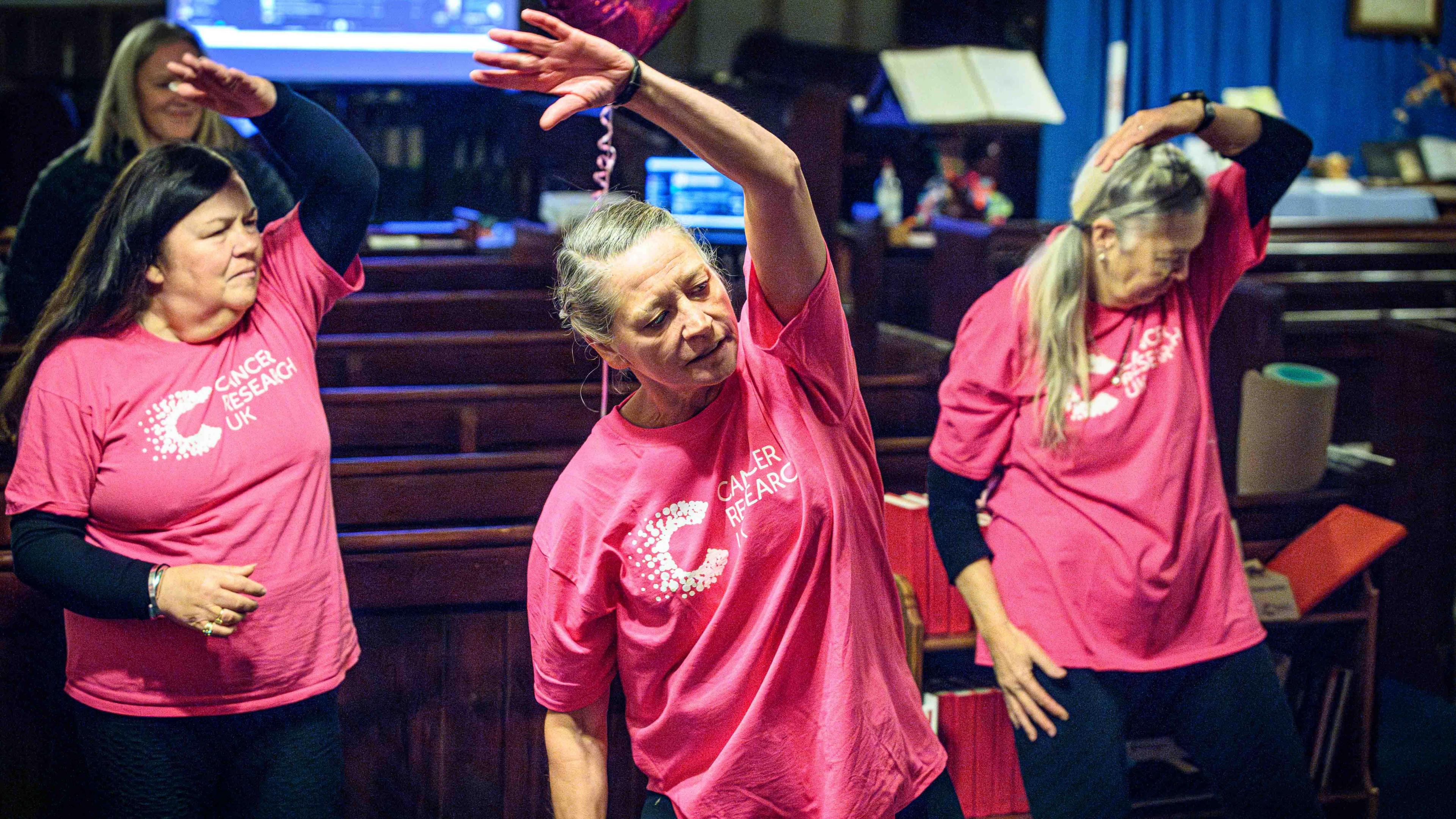 Three women in pink t-shirts stretch above their heads