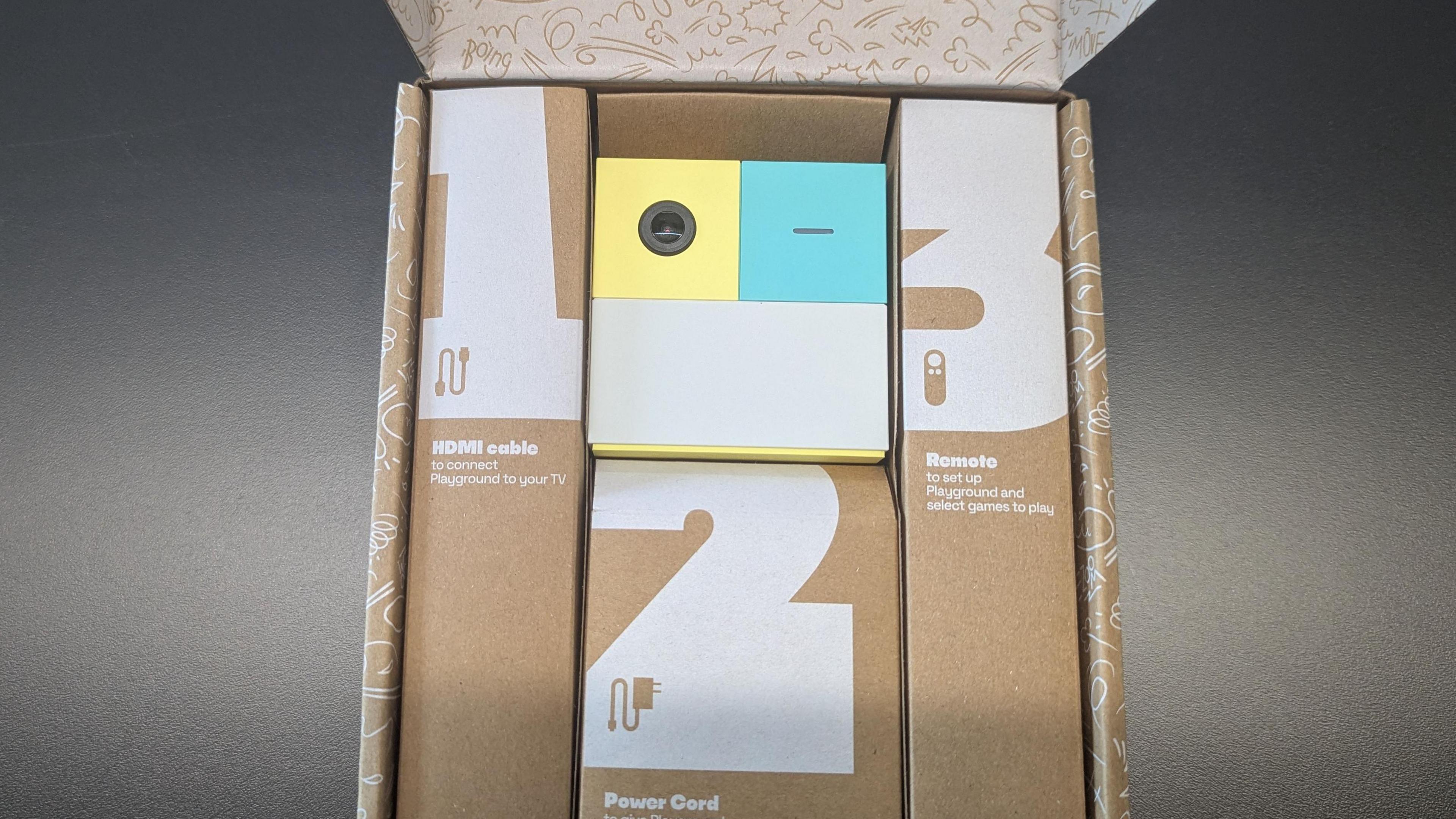 A beige box with three smaller boxes labelled 1 2 and 3 on them and the words HDMI cable, power cord and remote. In the middle is a small green white and turquoise cube with a camera lense.