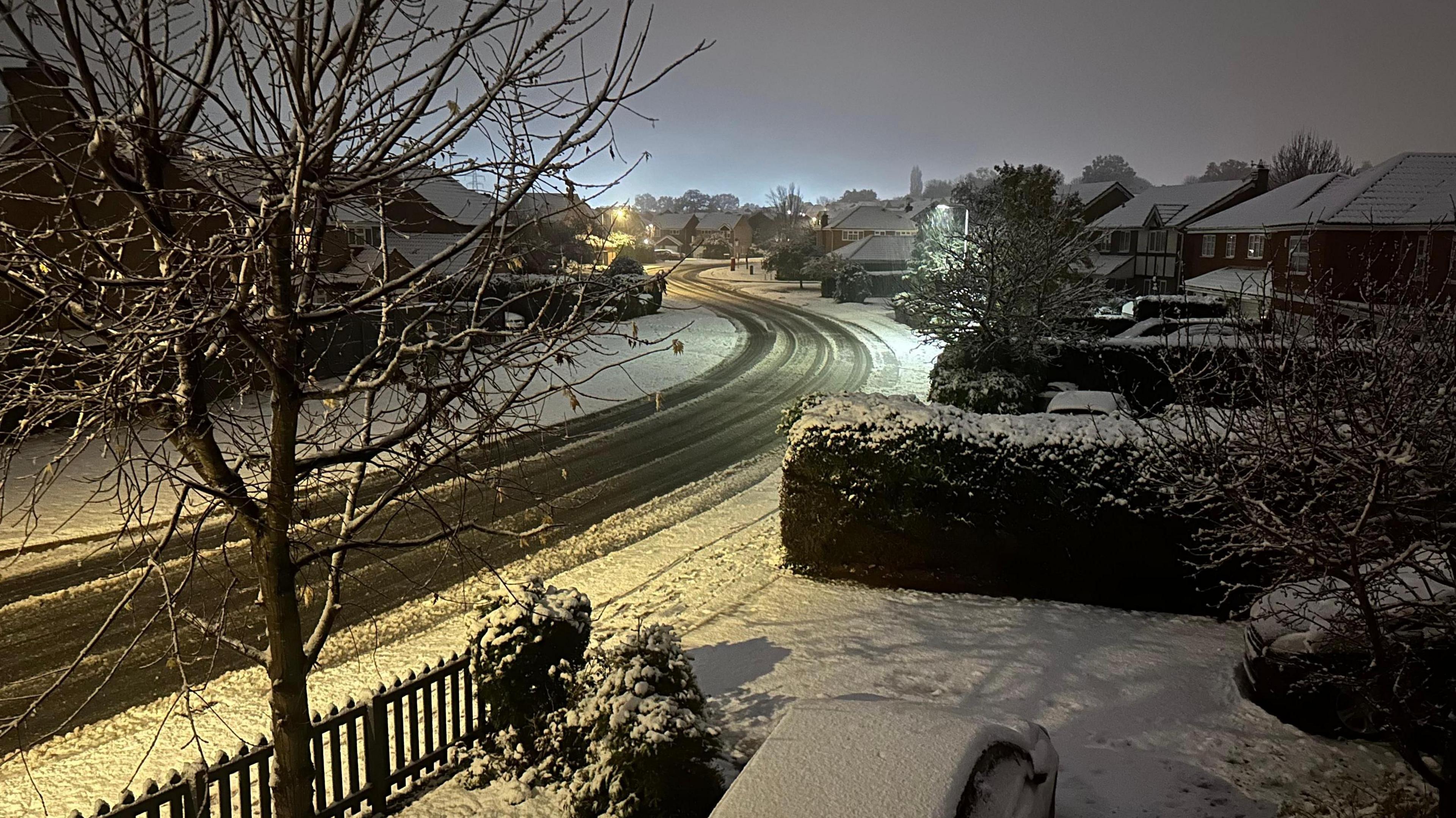 Snow-covered street in Grantham with houses and a tree in the foreground.