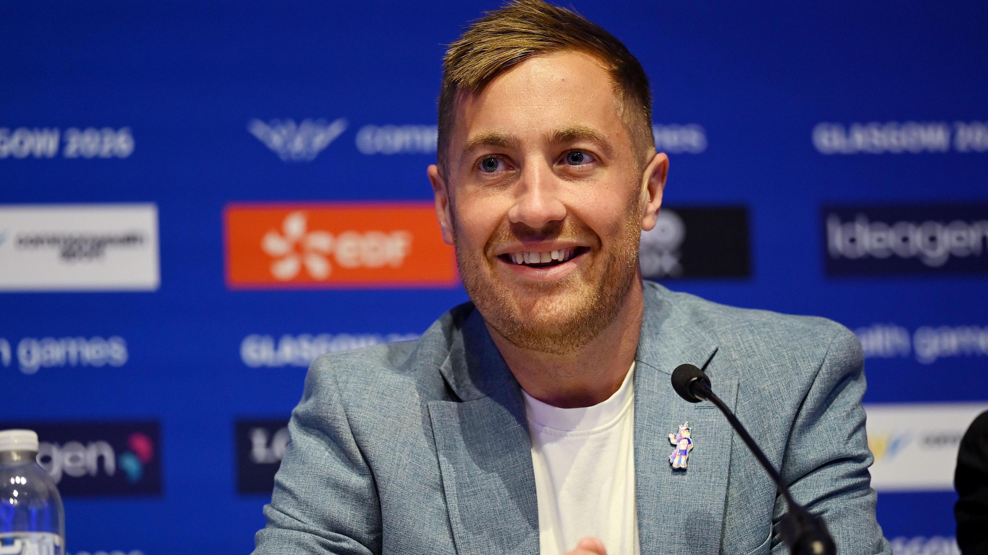 Phil Batty smiling. He is in a blue jacket and white T-shirt and has blonde hair.