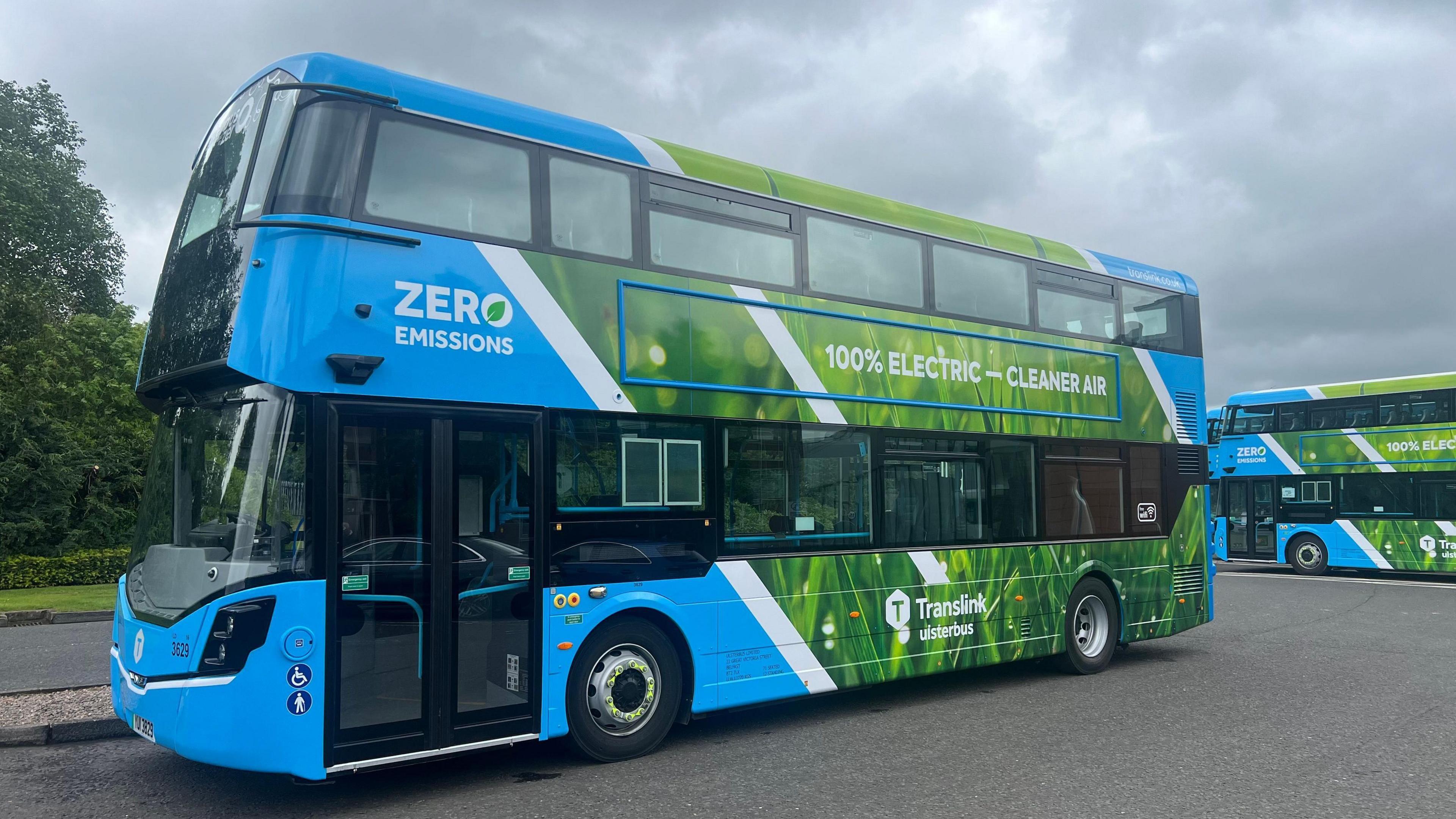 A side view of a double-decker electric bus in blue with the image of grass on its side