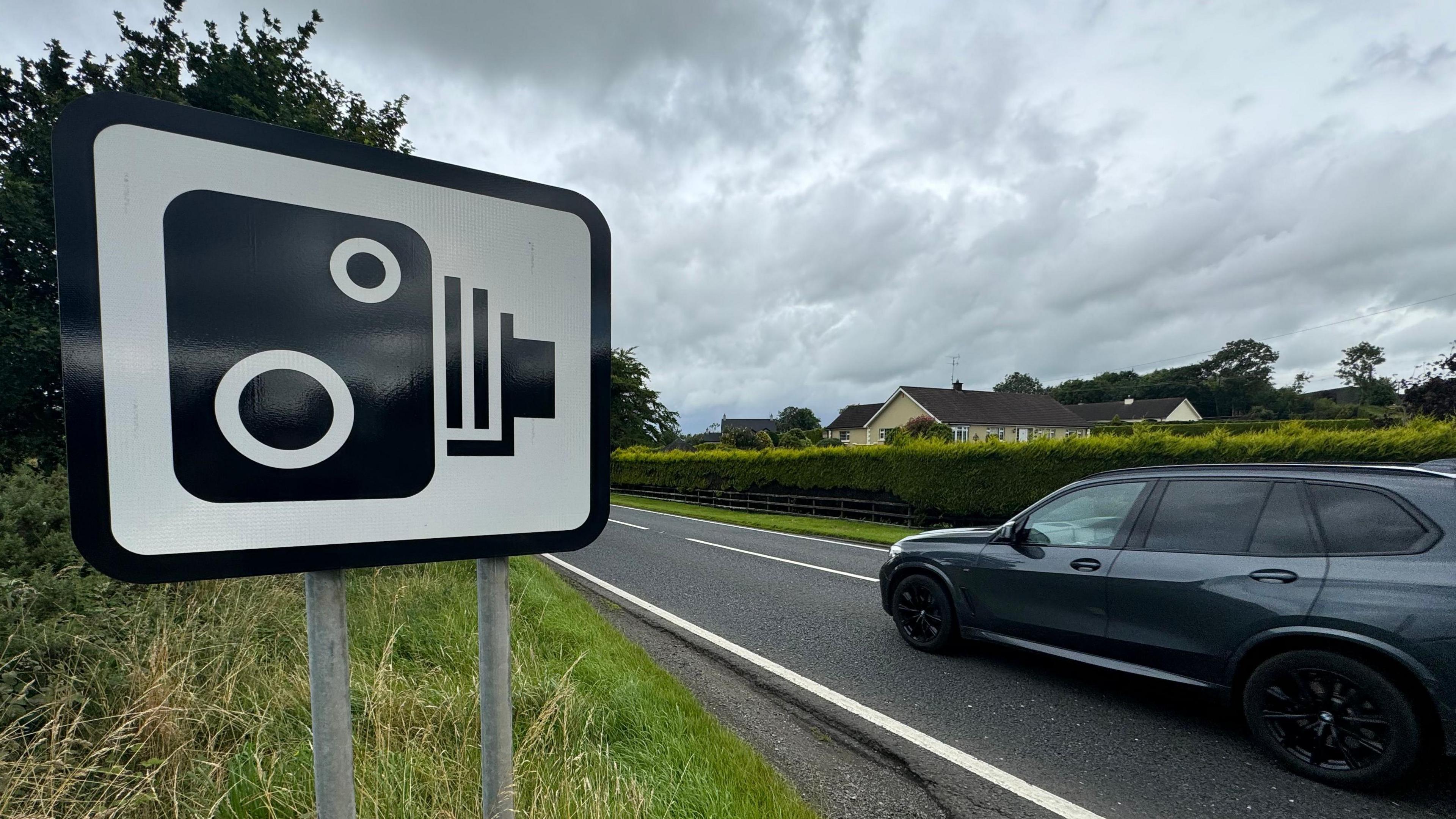 Image of a speed camera warning sign with a car driving past it. 