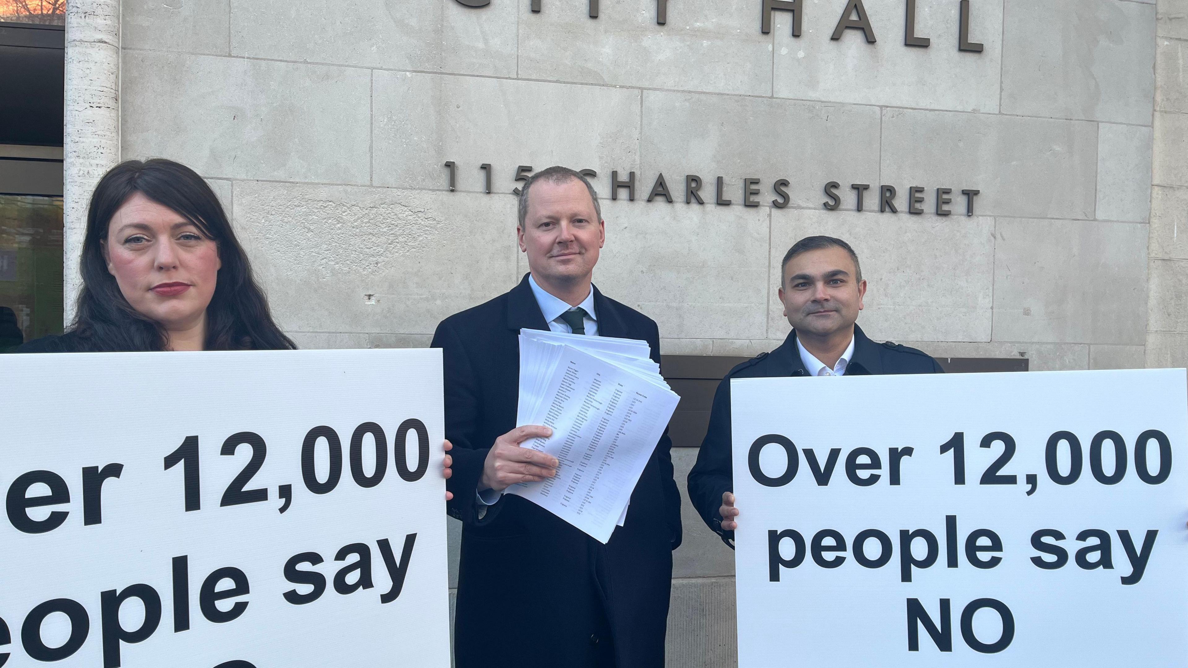 A woman and two men holding signs saying "Over 12,000 people say no" 