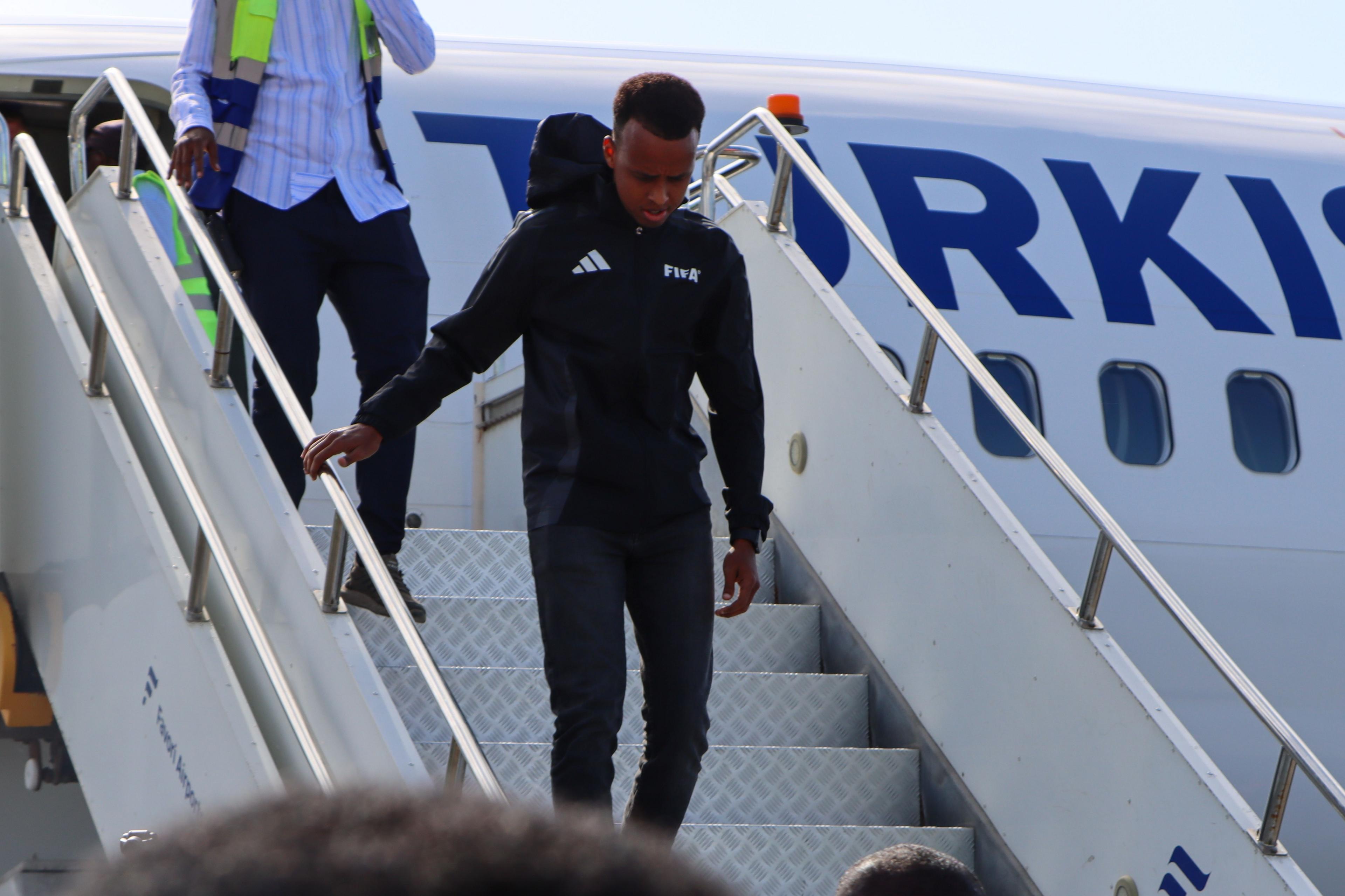 Omar Irfan, wearing a achromatic Fifa hoodie and trousers, walks down the achromatic metallic stairs from the achromatic Turkish Airlines plane