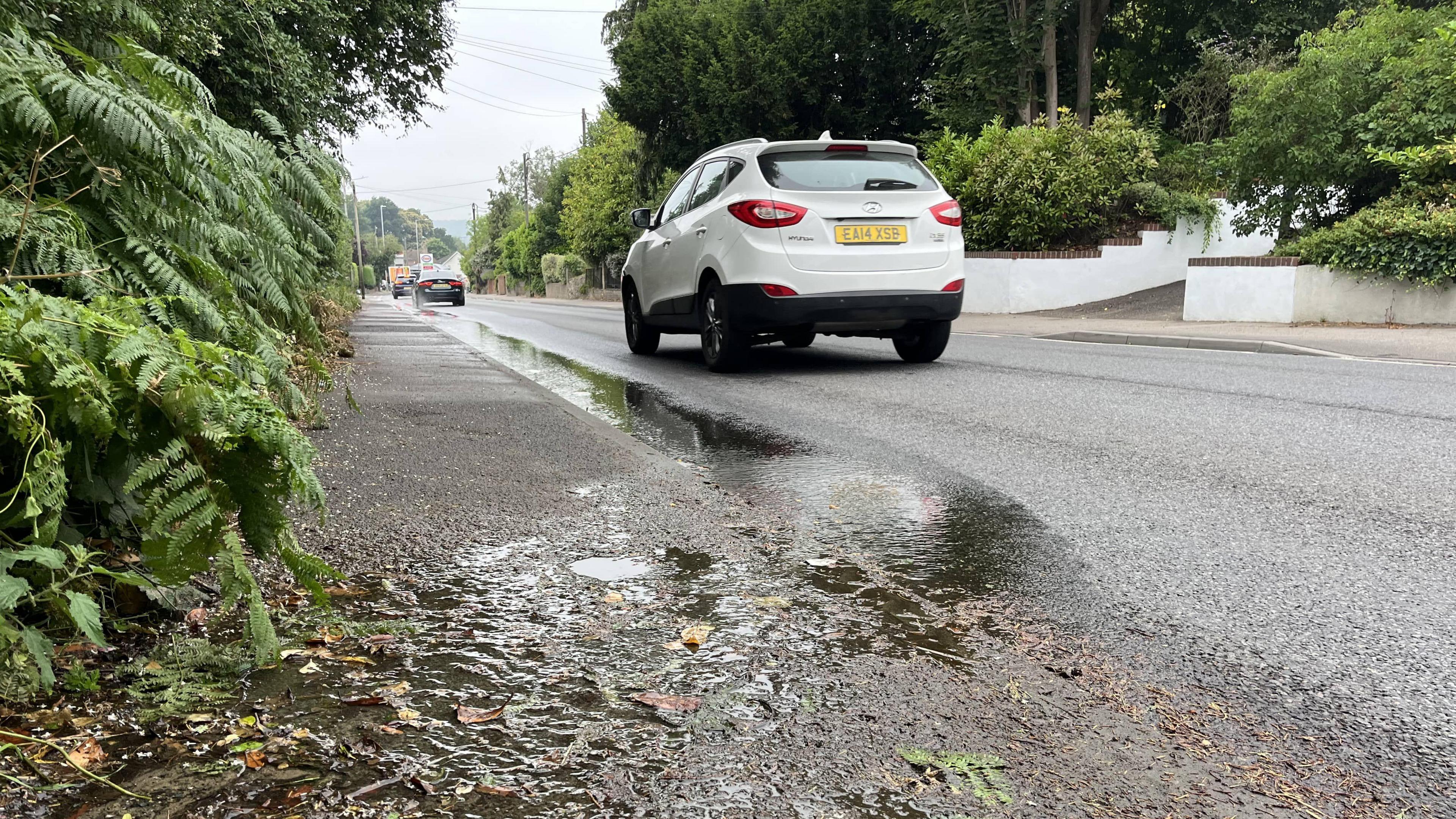 A stream of leaking water on the curb on Maidstone Road in Borough Green with a white car driving by
