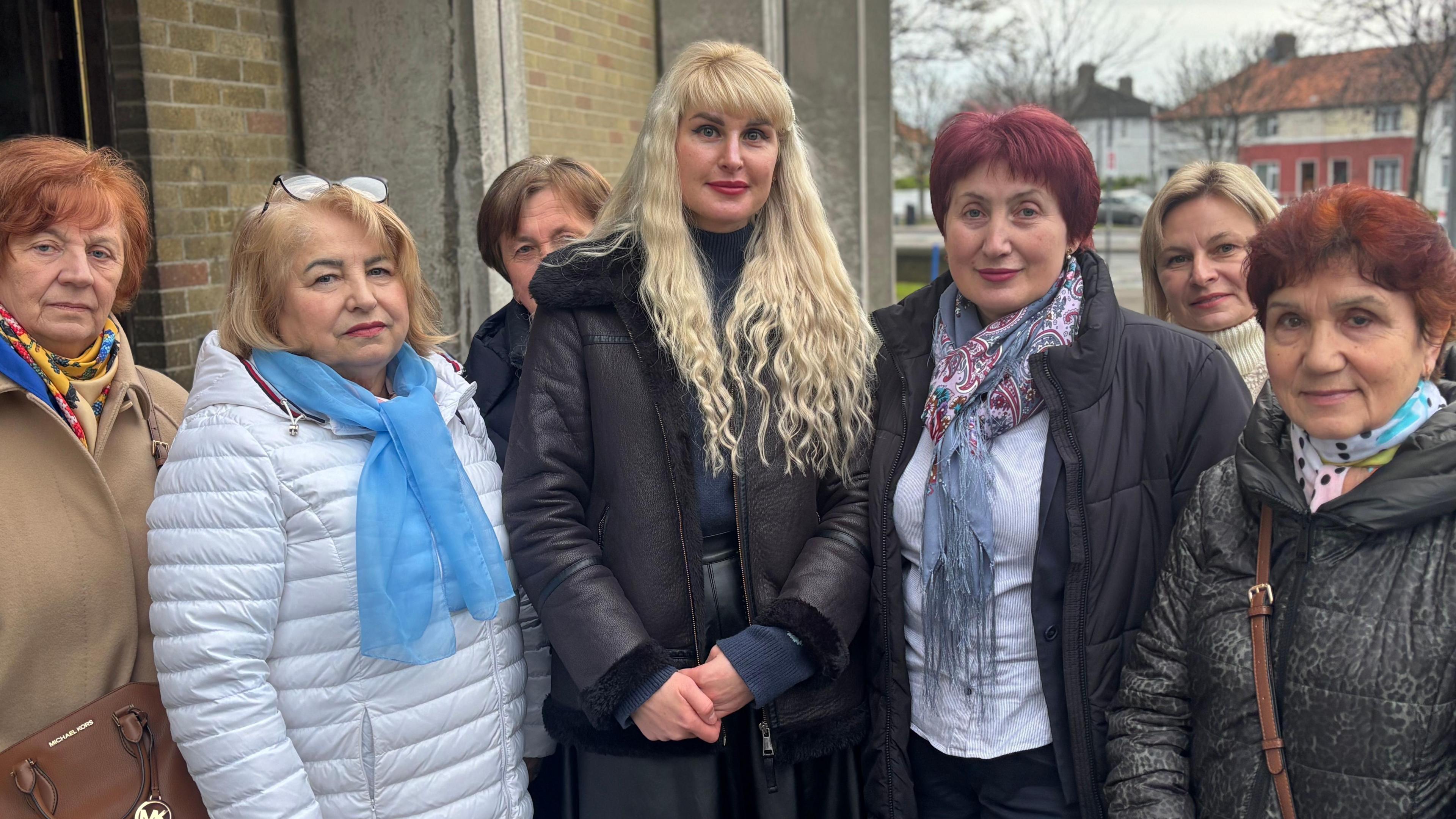 A group of Ukrainian women standing outside of a church wearing winter coats smile at the camera