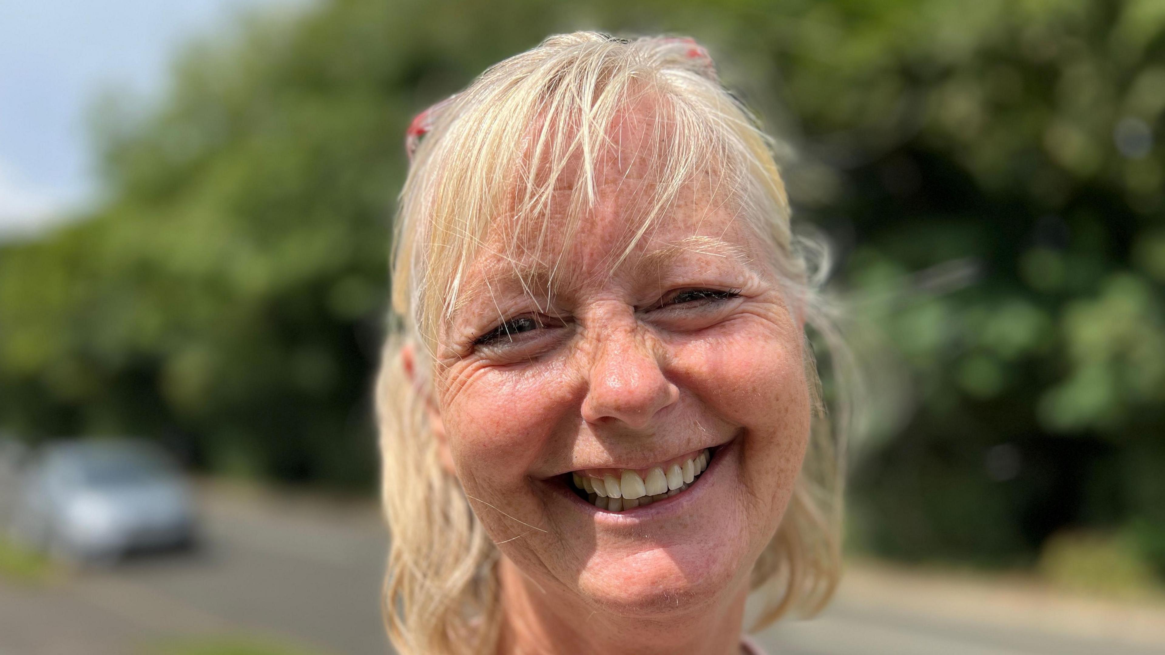 Blonde-haired Alison Cann smiles for the camera with a blurred out road behind her