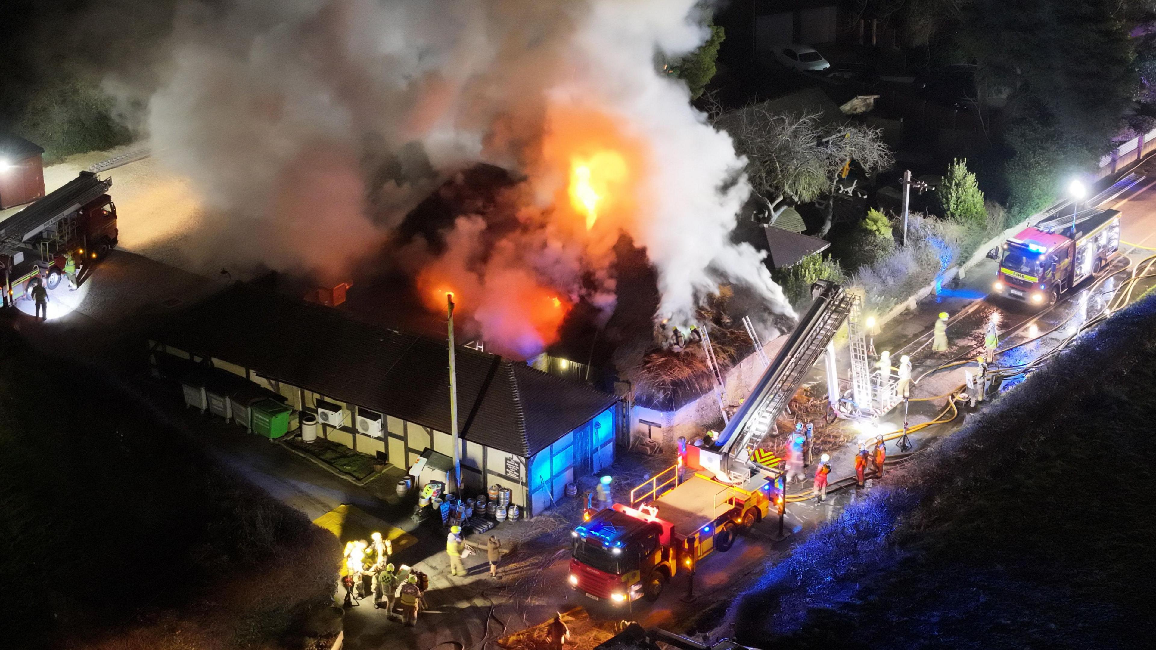 Fire crews tackling a fire in a pub building with flames and smoke billowing from the roof.