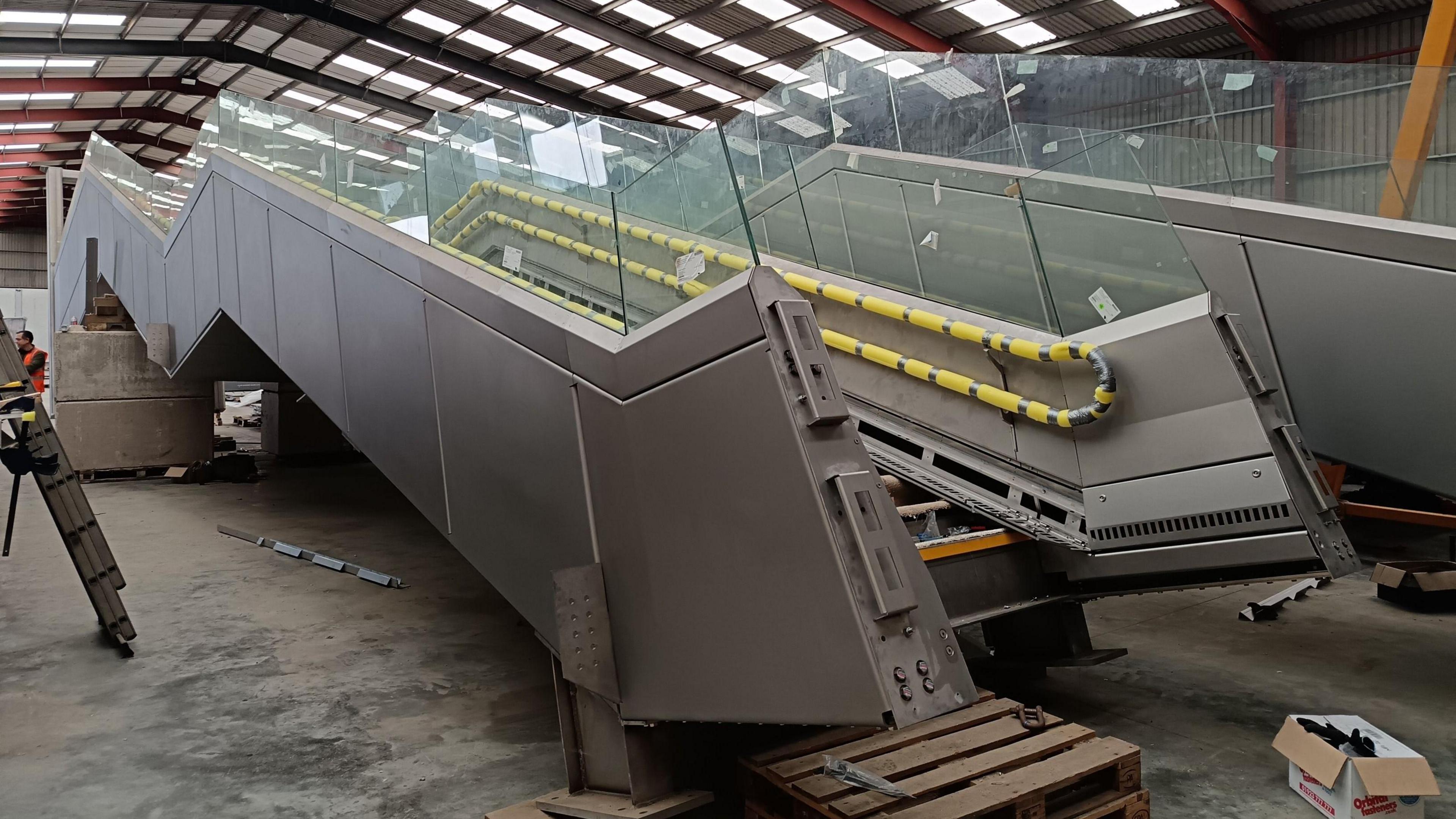 The stairs of the bridge inside a warehouse. They are stainless steel and rest at an angle inside the warehouse.
