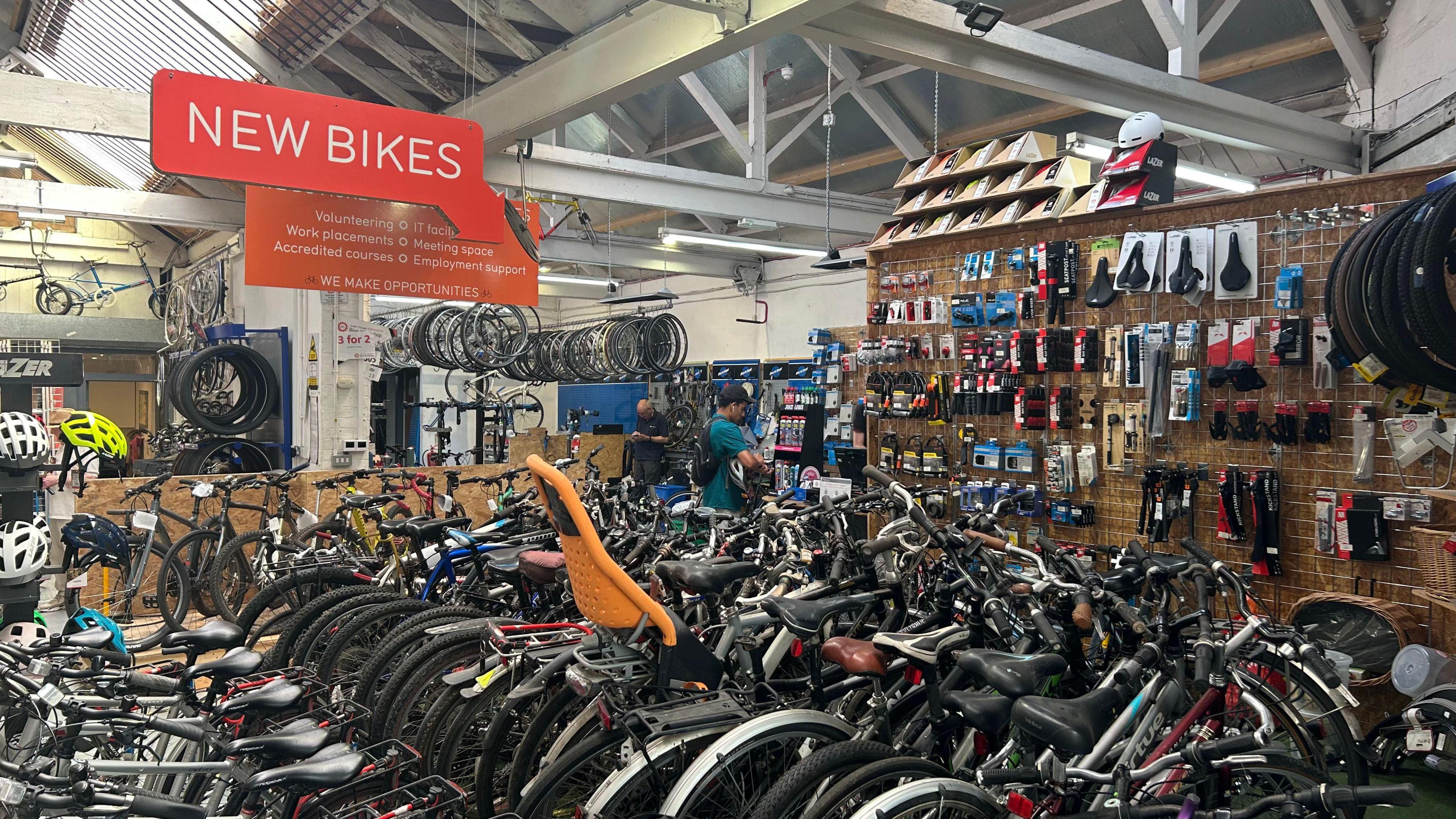 A variety of bikes lined up inside a shop with a sign that reads "new bikes" hanging from the roof.