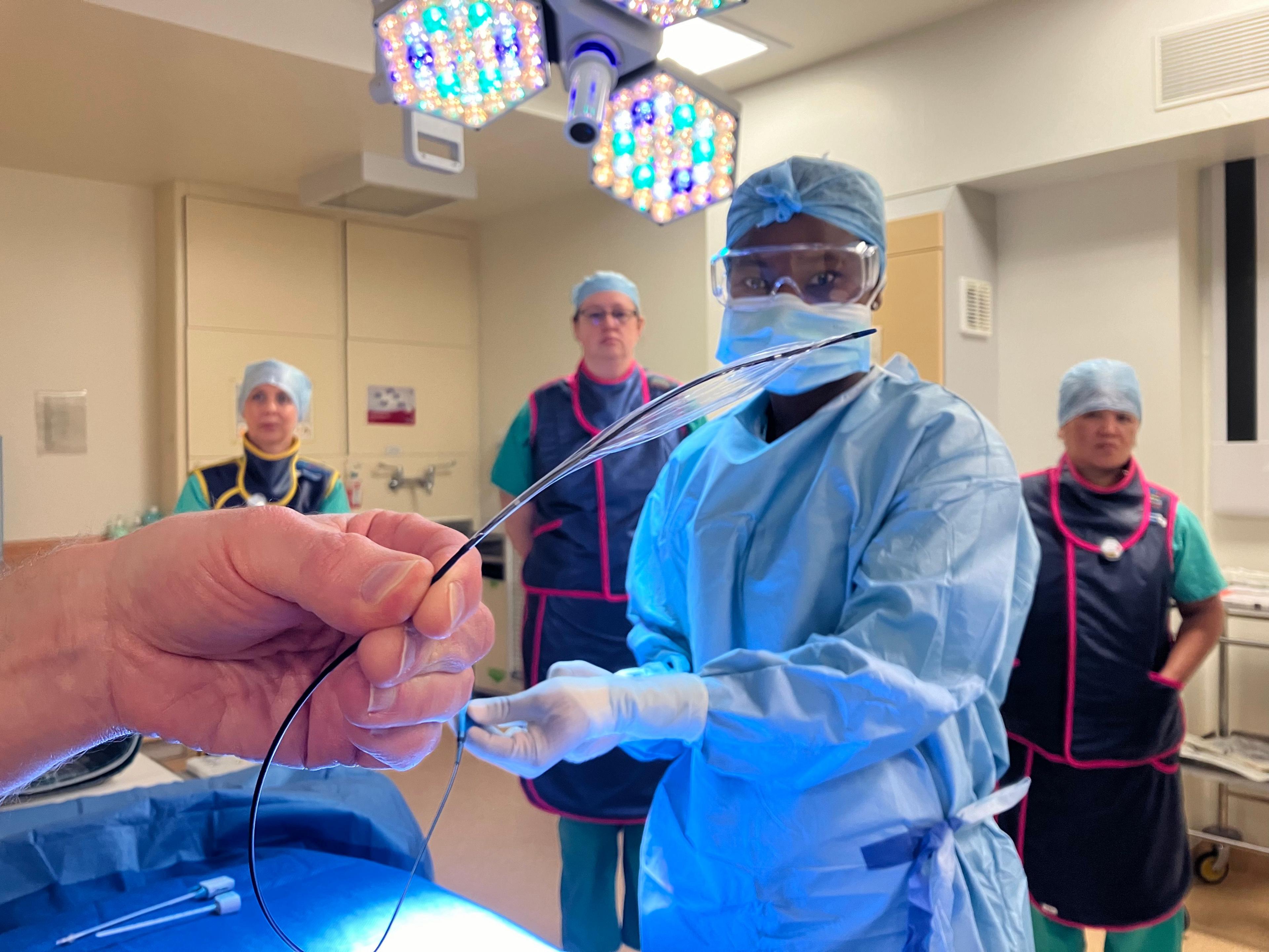 A staff member at the Queen's Medical Centre holds up a thin tube, while colleagues watch in the background