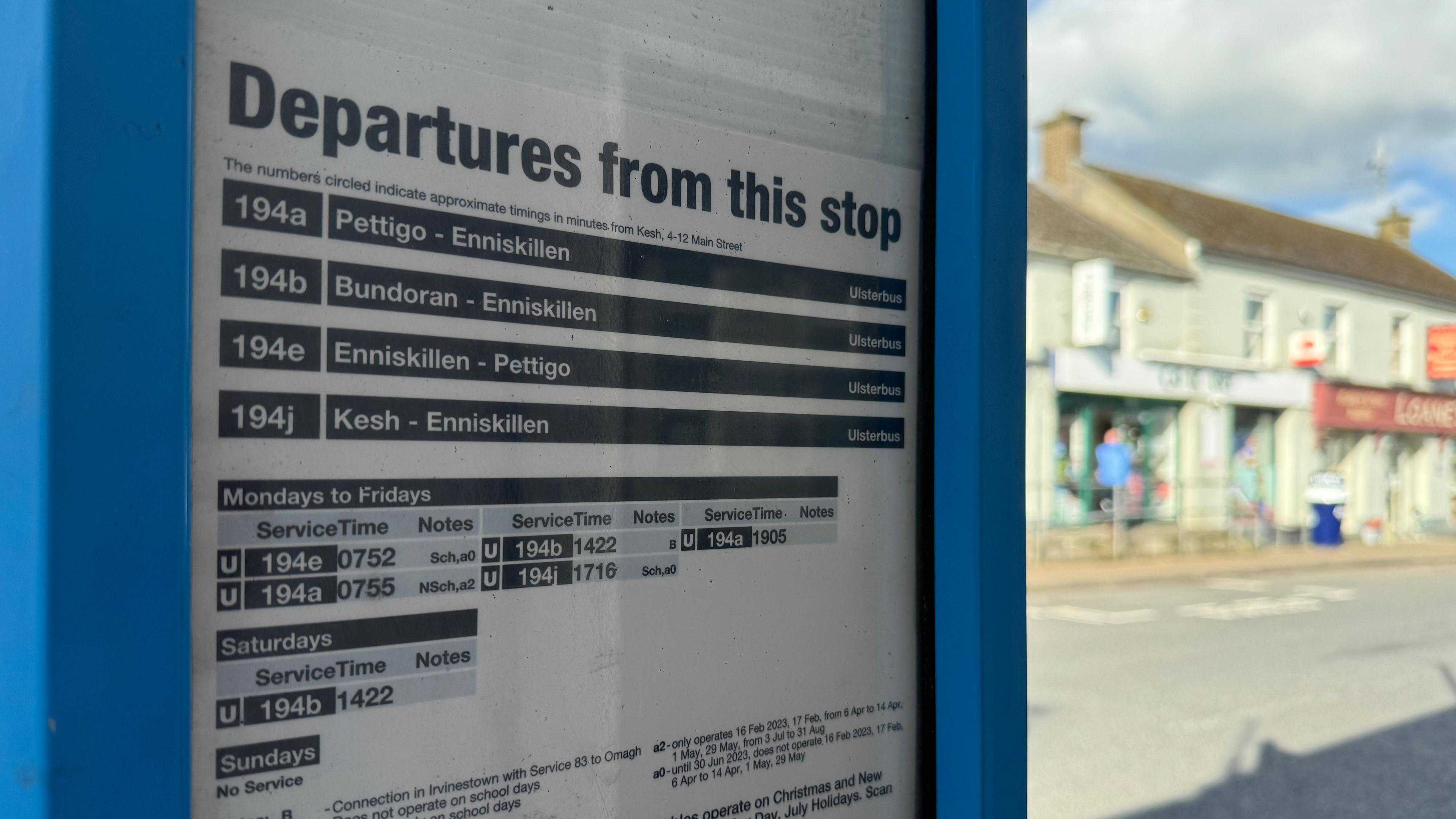 Close-up image of bus stop timetable of Kesh, County Fermanagh, with village shops in the background 