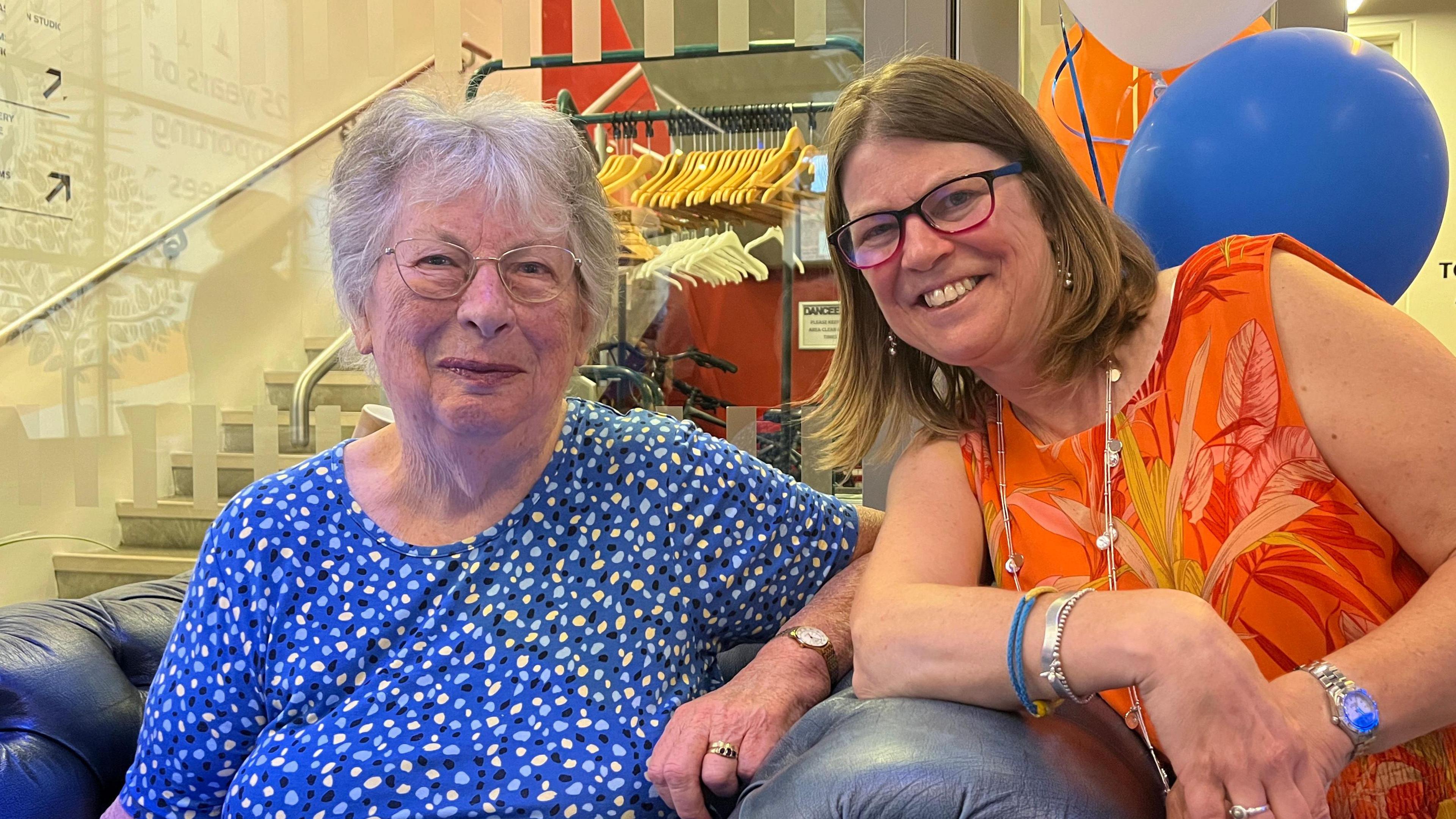 Cynthia Capey, a blue dress, and Rebecca Crerar in an orange top, with ballons behind them