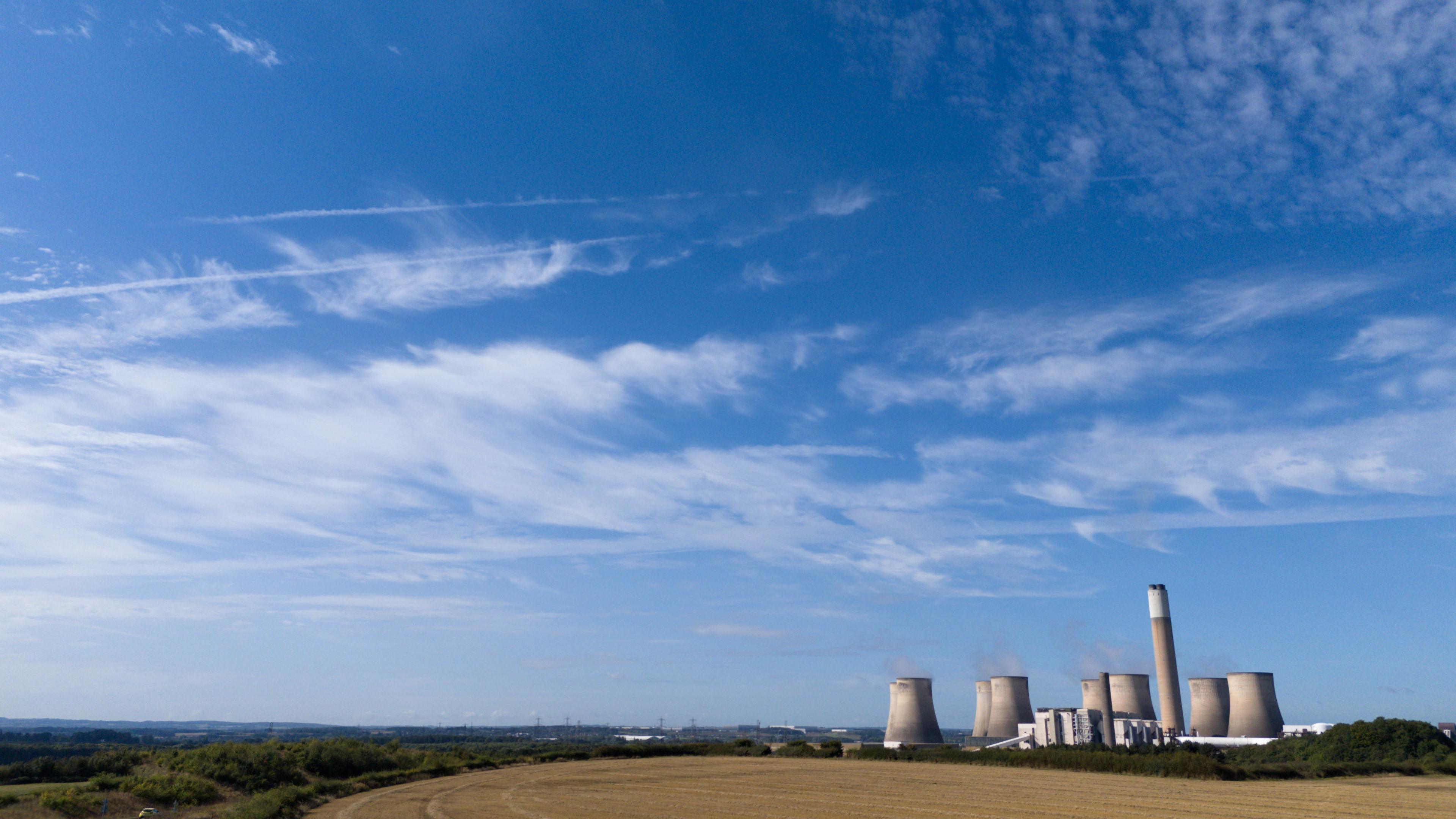 Ratcliffe-on-Soar power station in the middle distance, with blue skies overhead and fields surrounding it