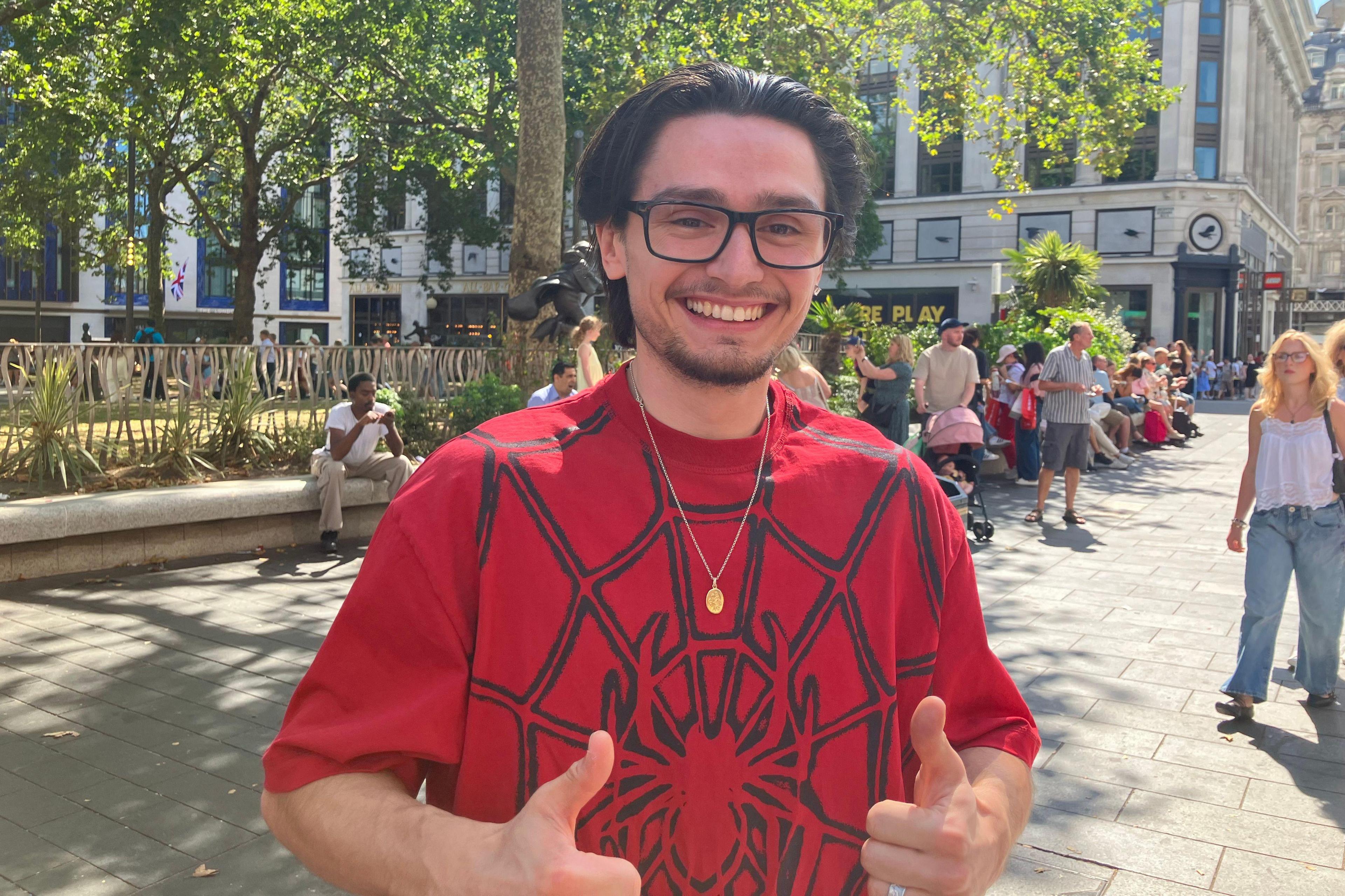 A Spider-Man fan wearing a red Spider-Man t-shirt stands with his thumbs up after seeing the film
