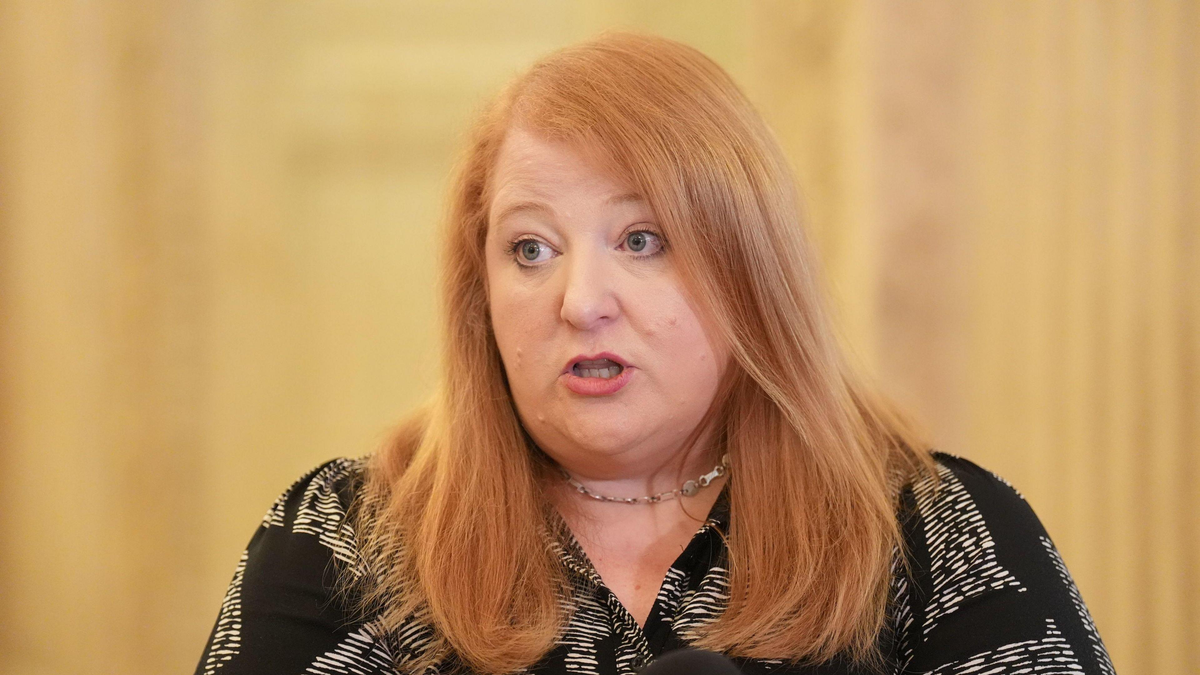 Naomi Long. She has long red hair, wearing a silver necklace and black and white blouse.