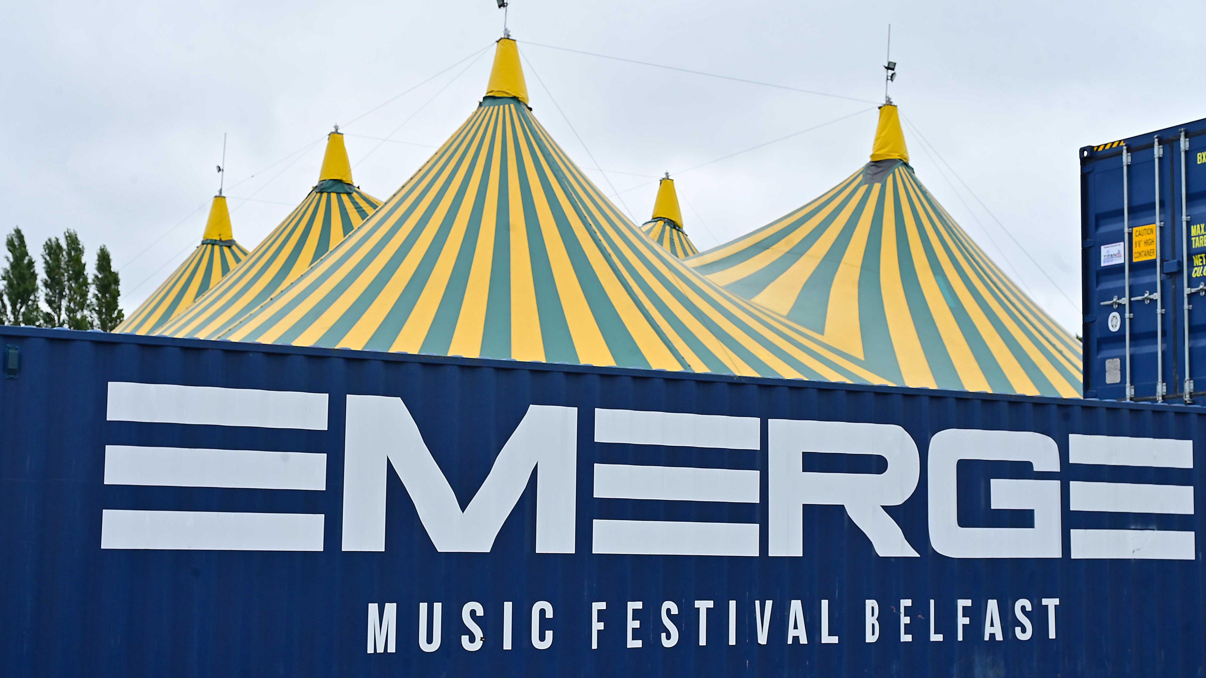 A green and yellow tent behind a shipping container with Emerge printed on the side of it