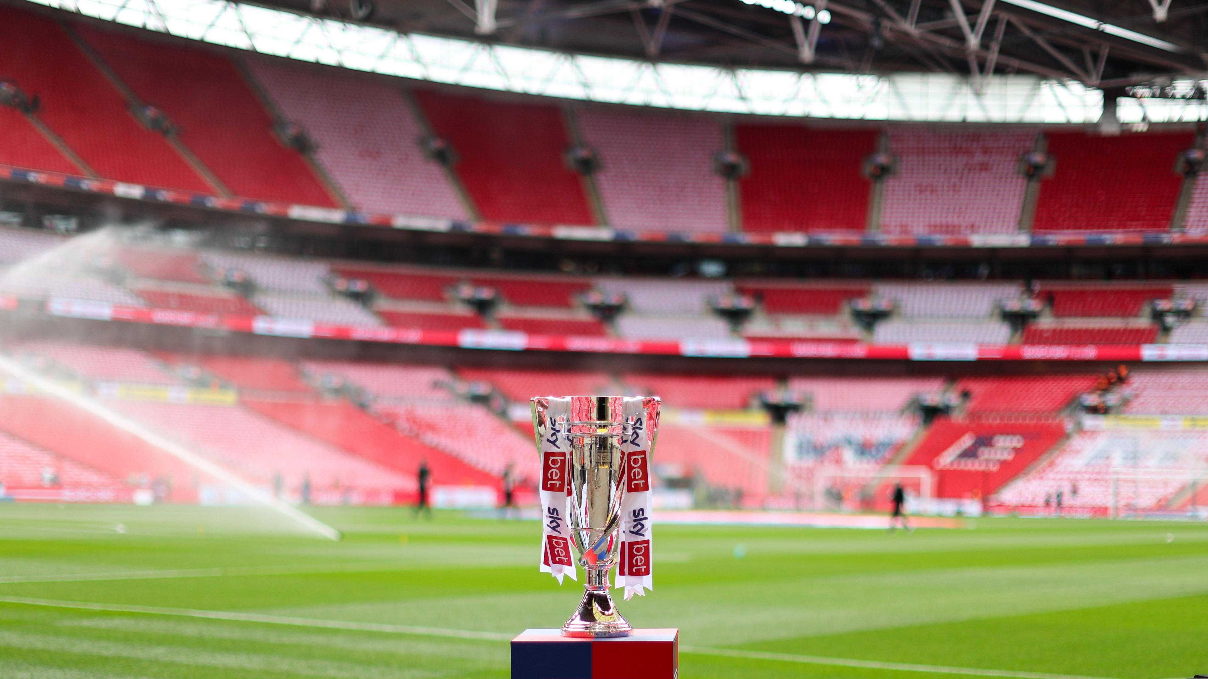 The Championship play-off final trophy on a stand at Wembley Stadium with the pitch and red seats visible behind