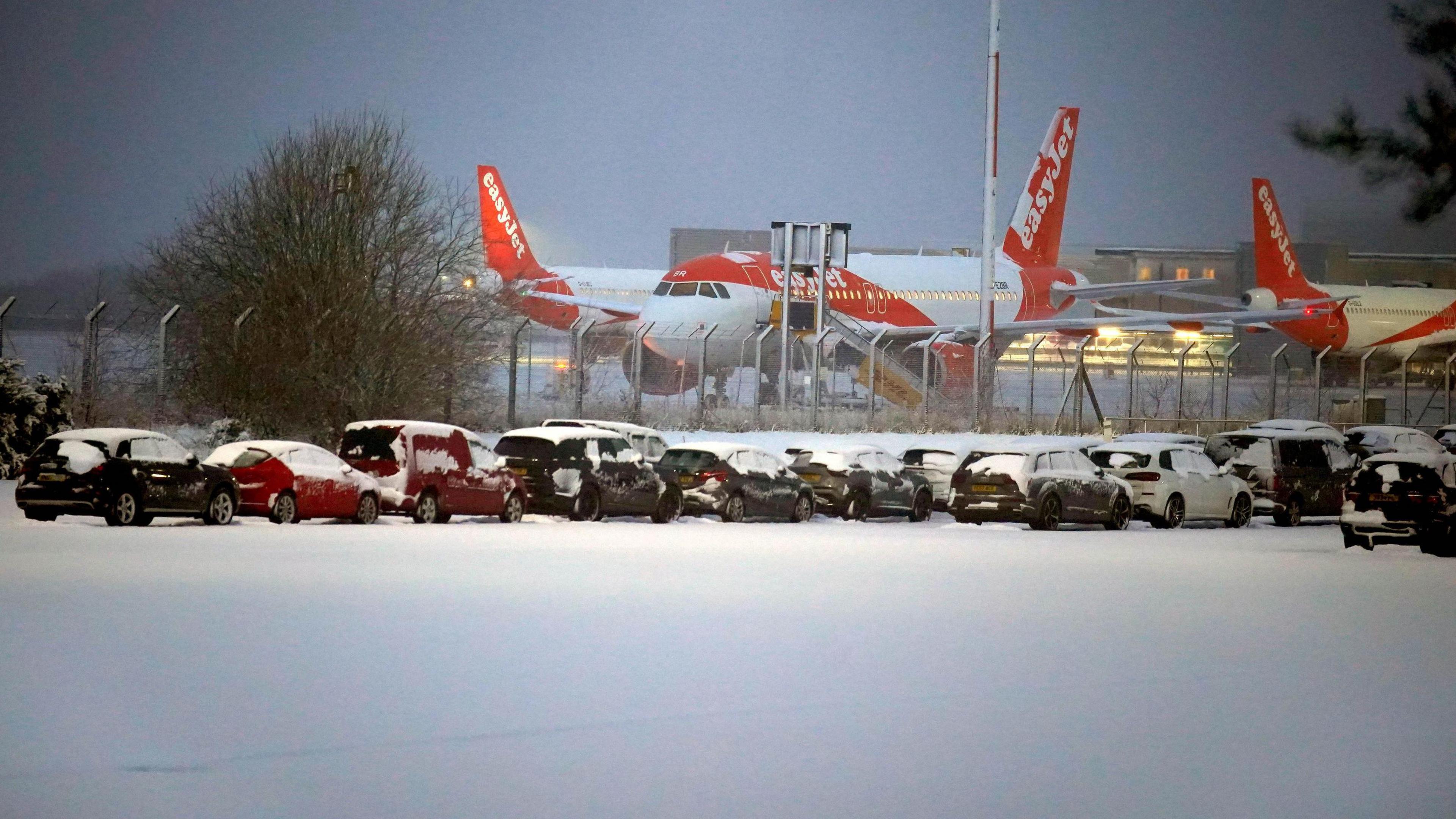 Planes on the tarmac behind a snow-laden car park 